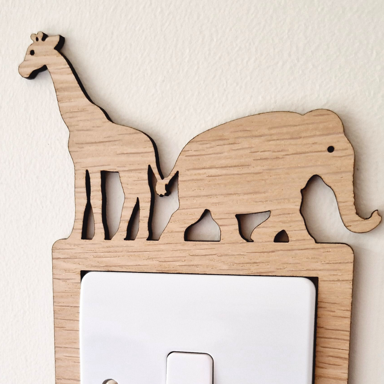 A wooden light switch with a giraffe and elephant silhouette on top, mounted on a white wall.