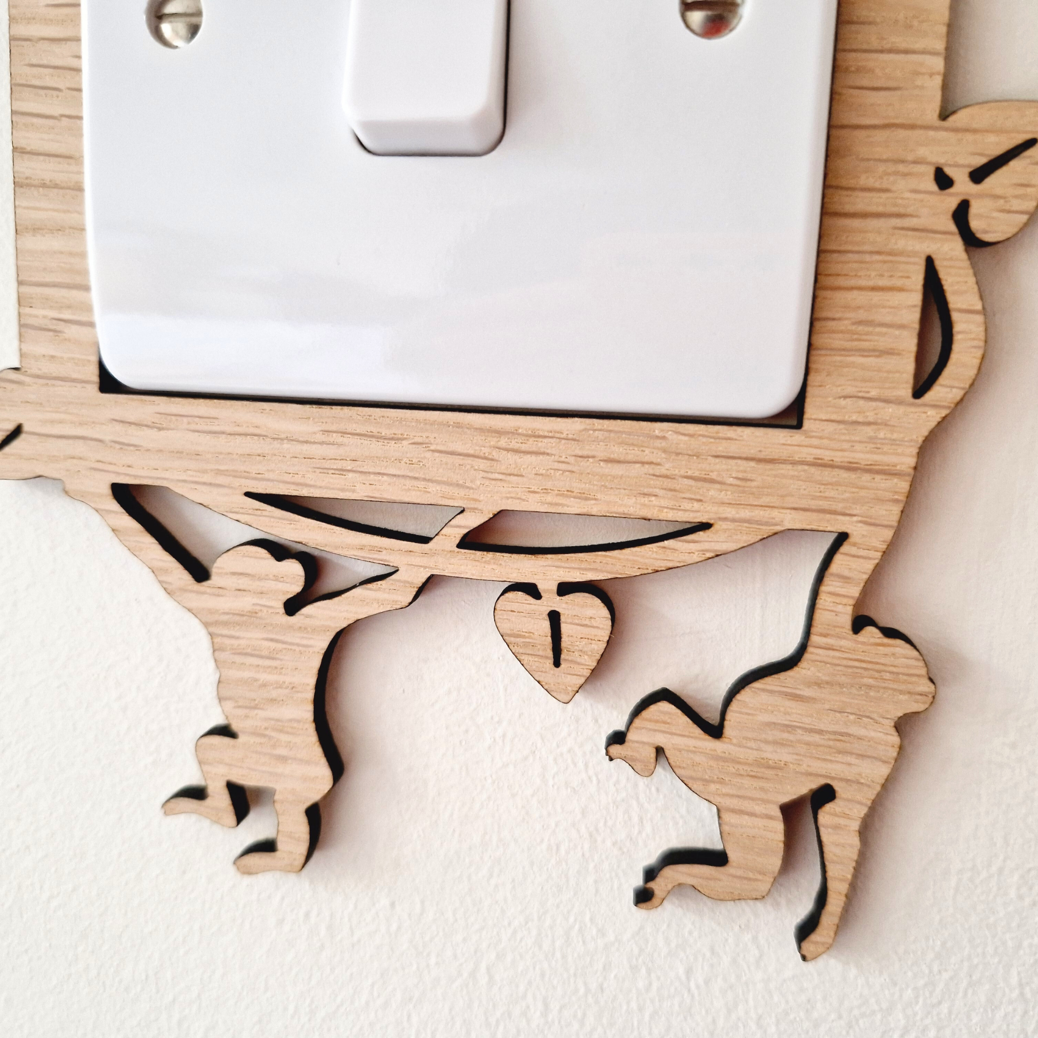 A wooden light switch cover with a carved design depicting two monkey figures.