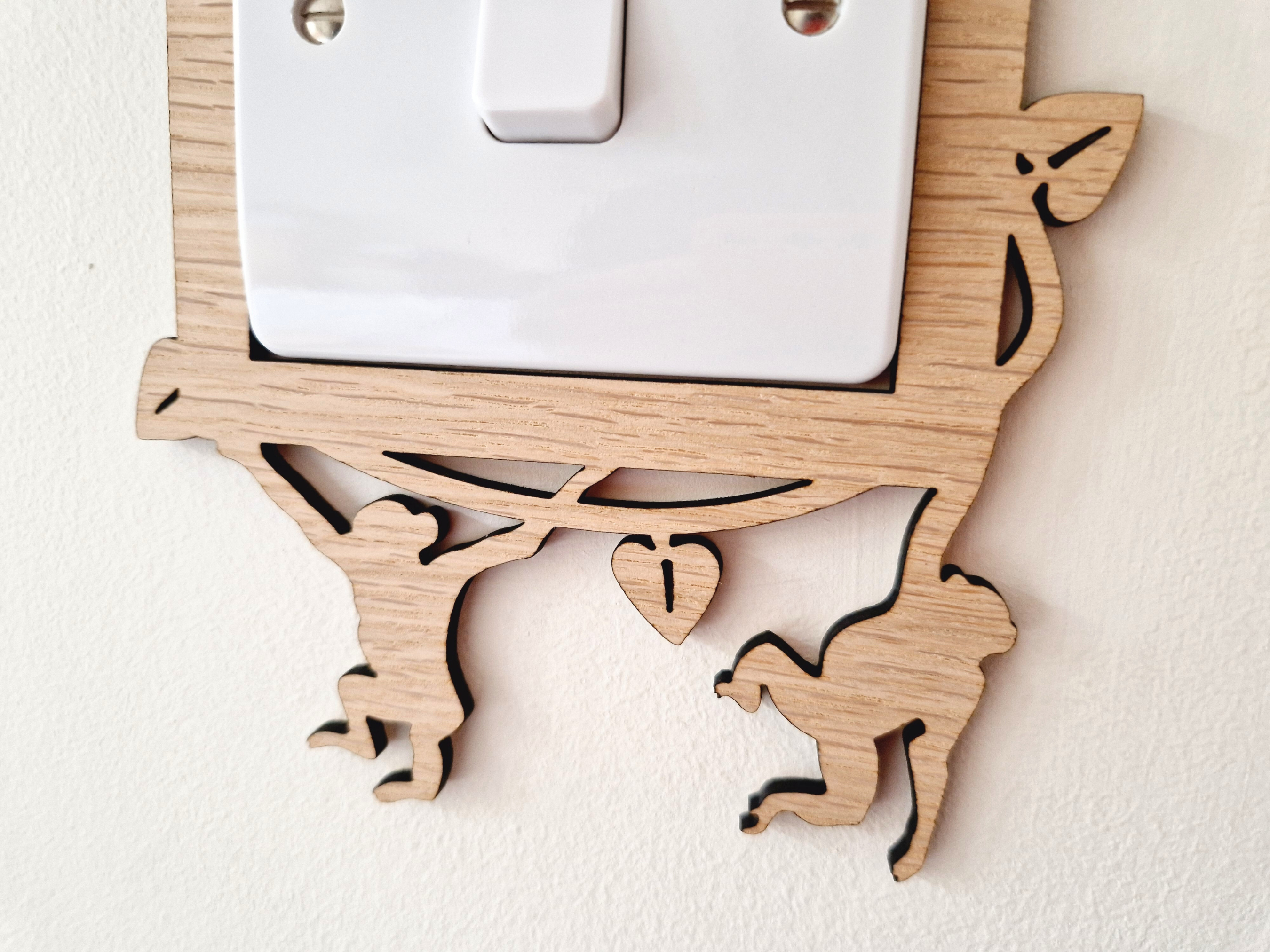 A wooden light switch cover with a carved design depicting two monkey figures.