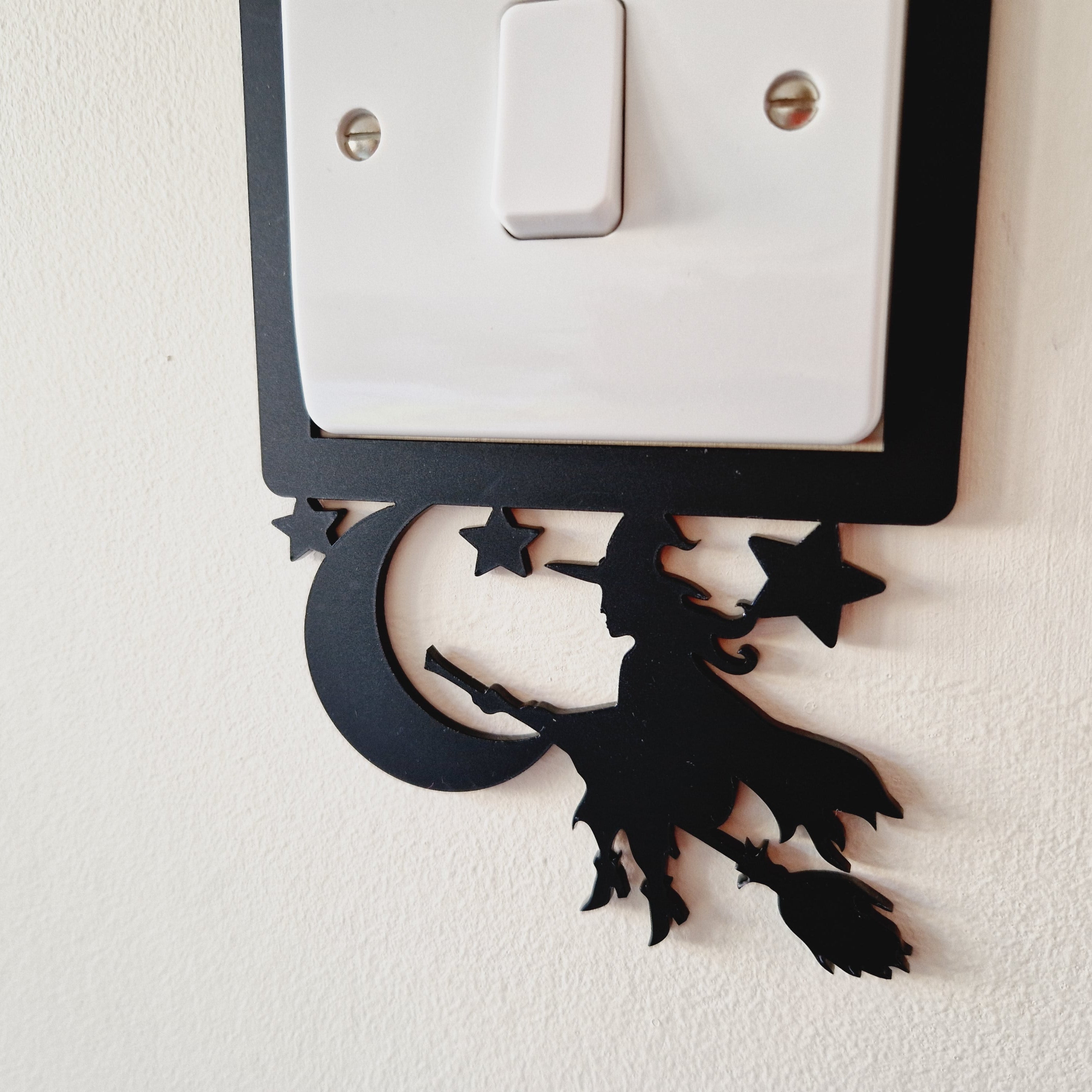 Decorative black silhouette of a witch on a broom, on a light switch cover