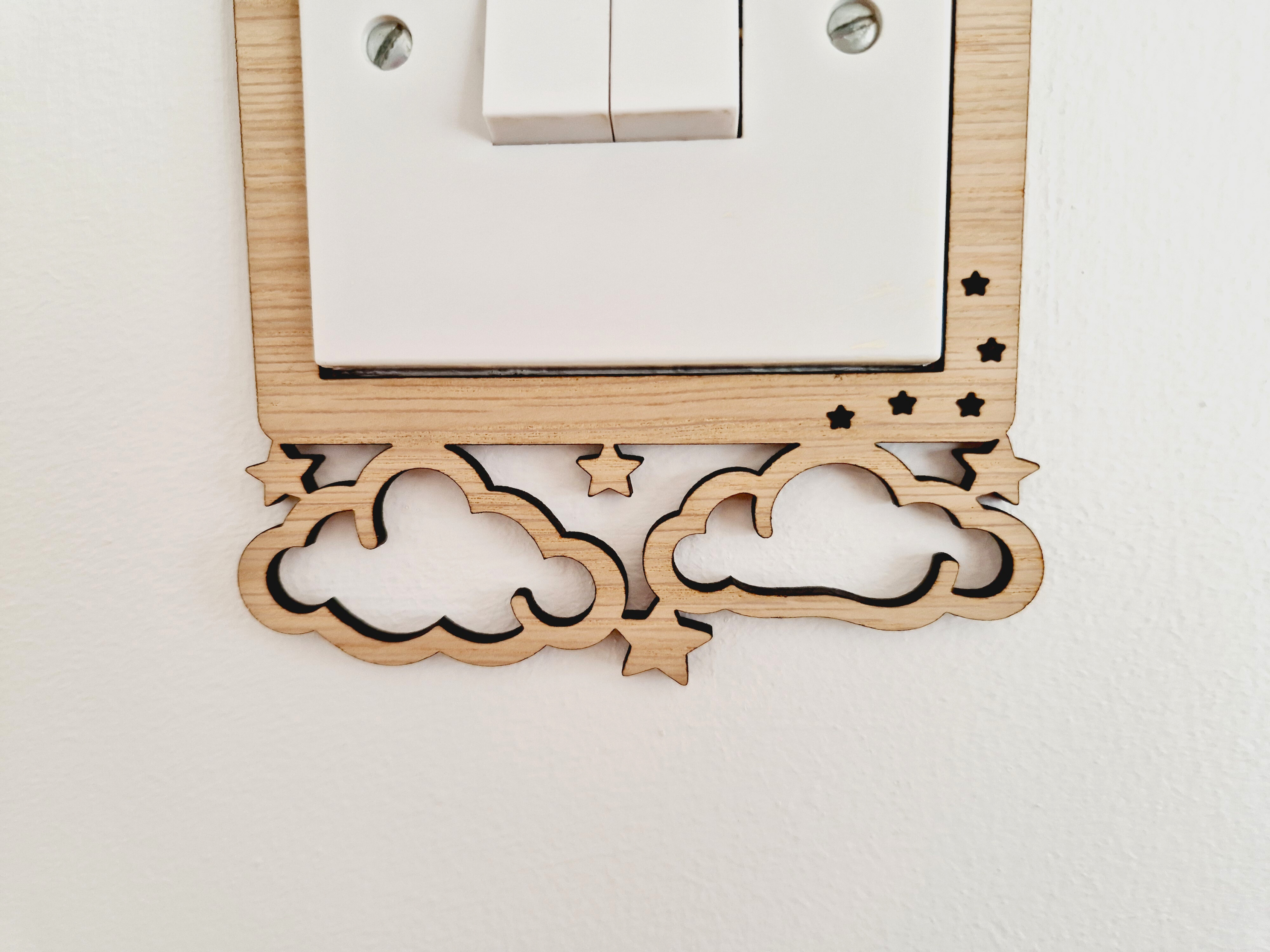a wooden light switch with a decorative design featuring clouds and stars carved into the switch itself.