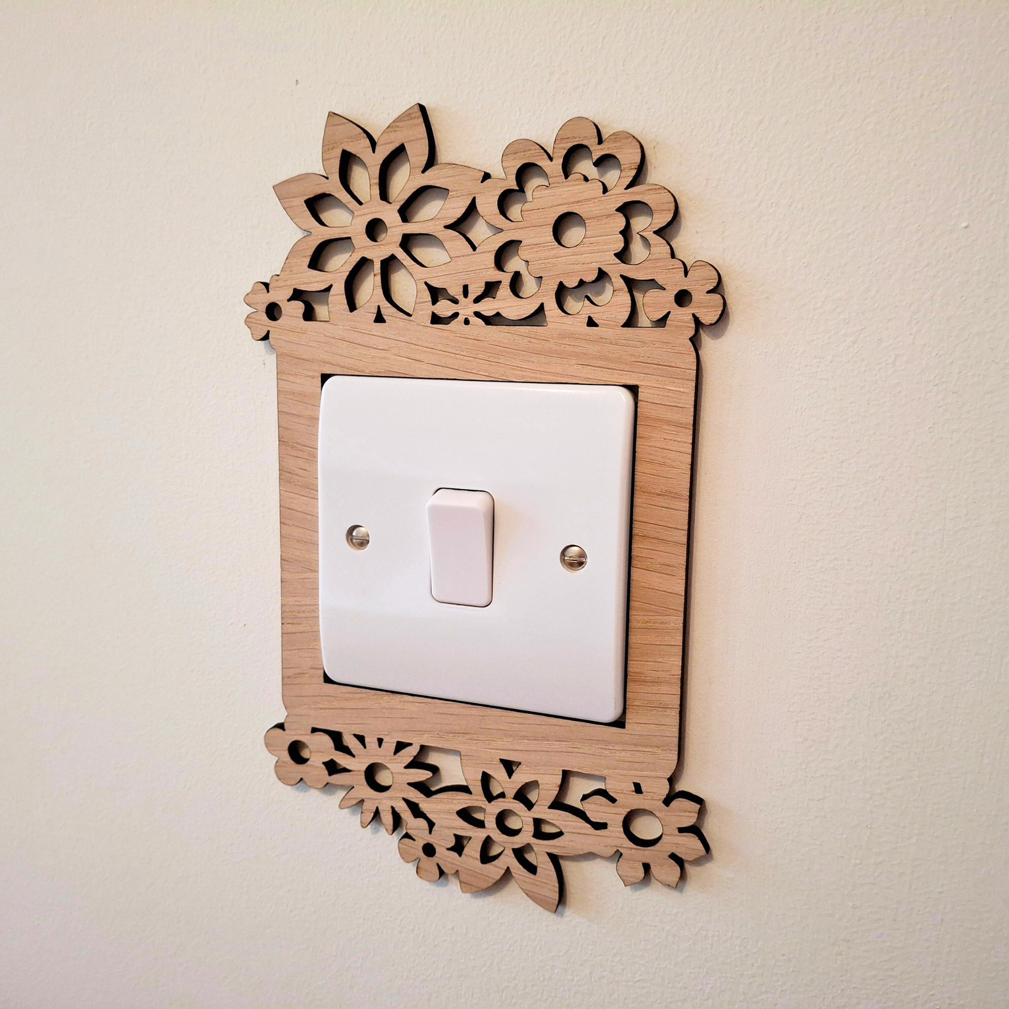 A wooden light switch with a floral design on the top and bottom edges, mounted on a wall.