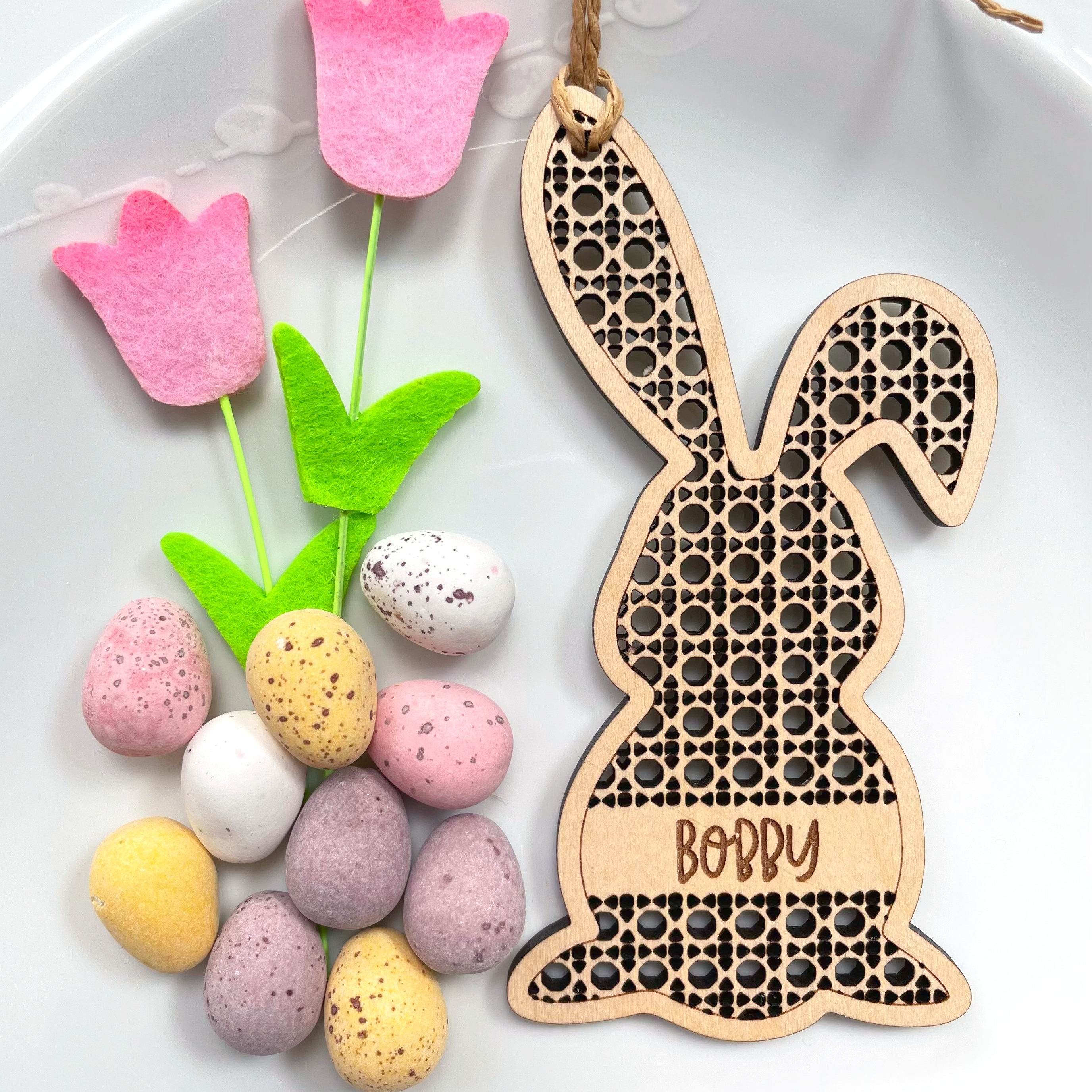 a wooden Easter bunny decoration hanging on a wall, surrounded by colorful Easter eggs and pink felt flowers.