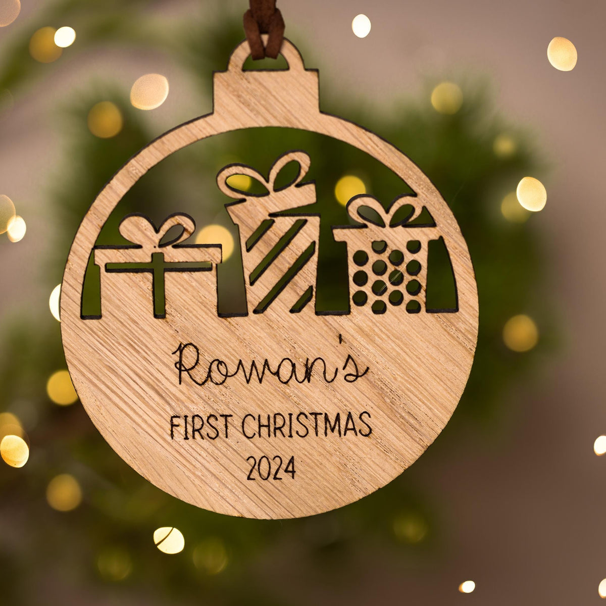 Wooden ornament with cut-out gift shapes and 'Rowan's First Christmas 2024' text, against a festive background.