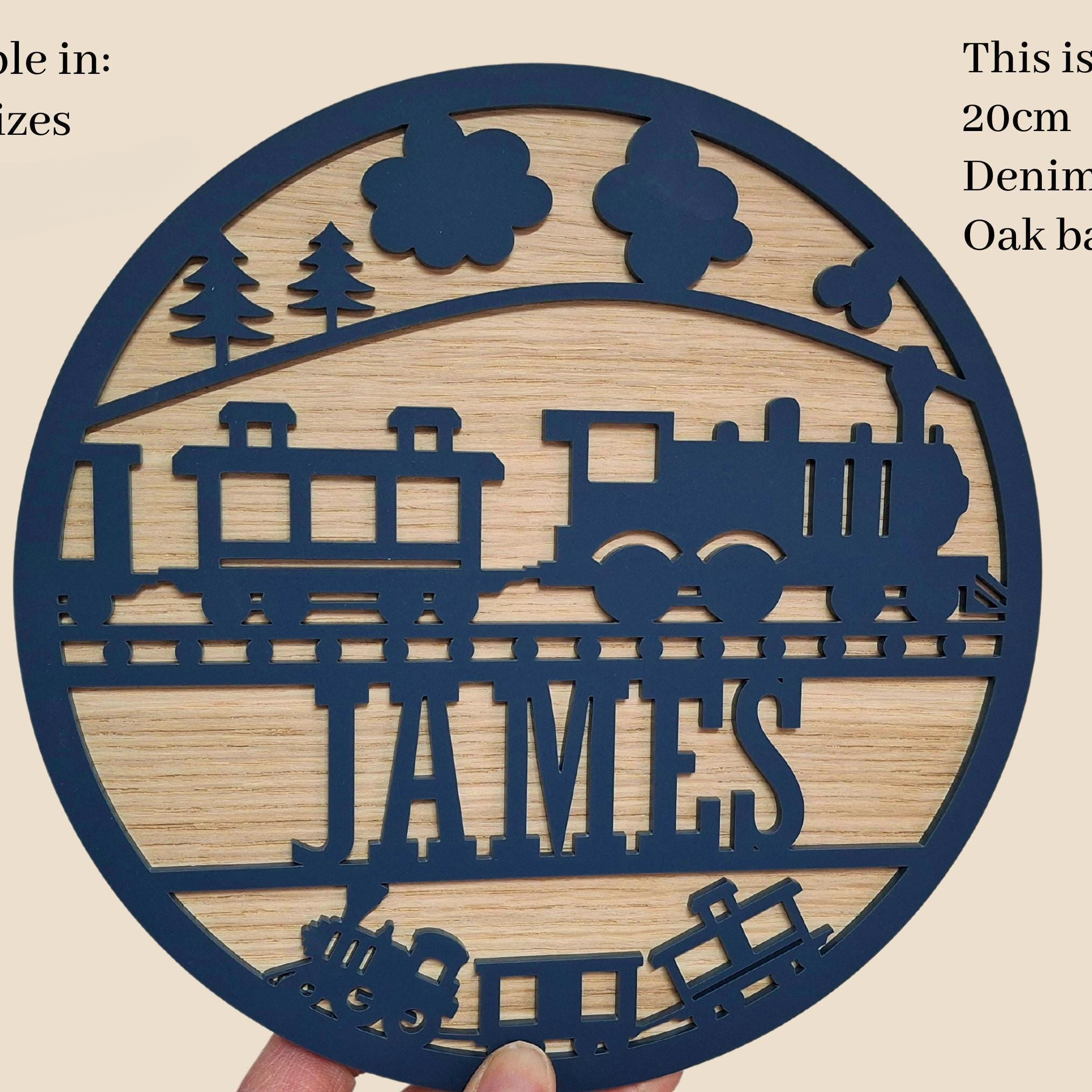 A hand holding a circular wooden sign with a train design and the name "JAMES" written on it.