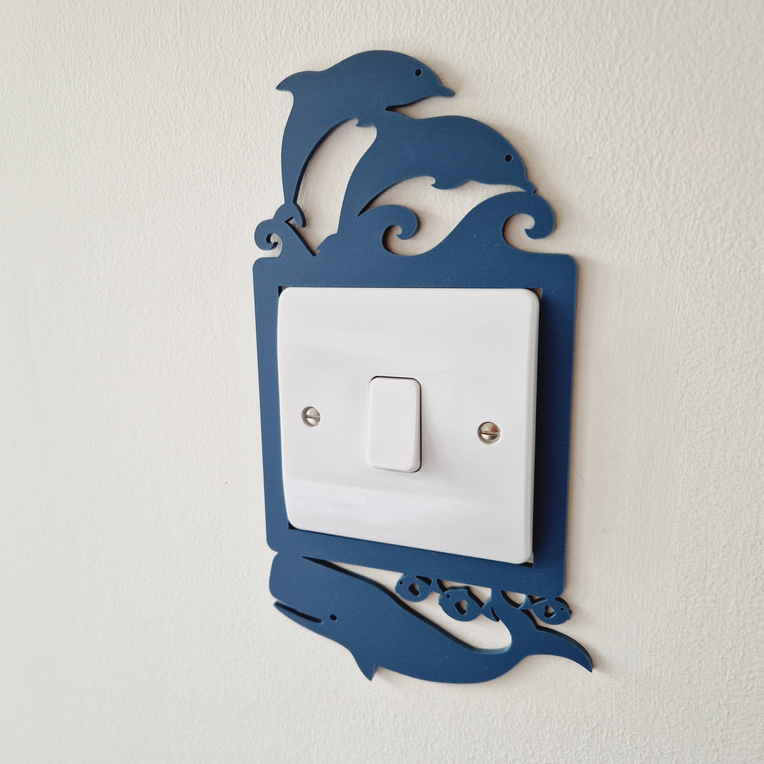 A light switch with a decorative blue frame featuring a playful design of two dolphins jumping in the air.