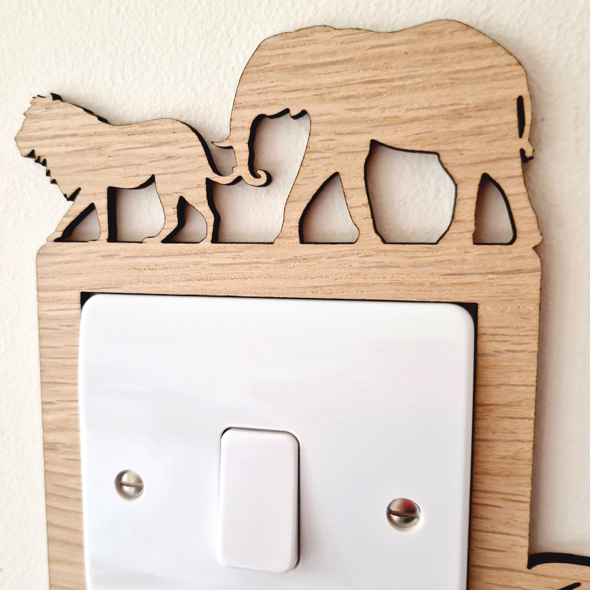A wooden light switch with a silhouette of an elephant and a lion on it.