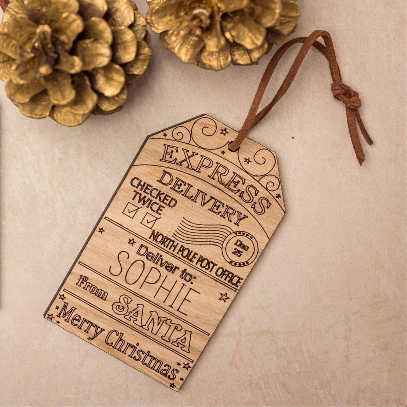 Christmas gift tags with personalized messages, surrounded by holly leaves and pine cones on a beige background.