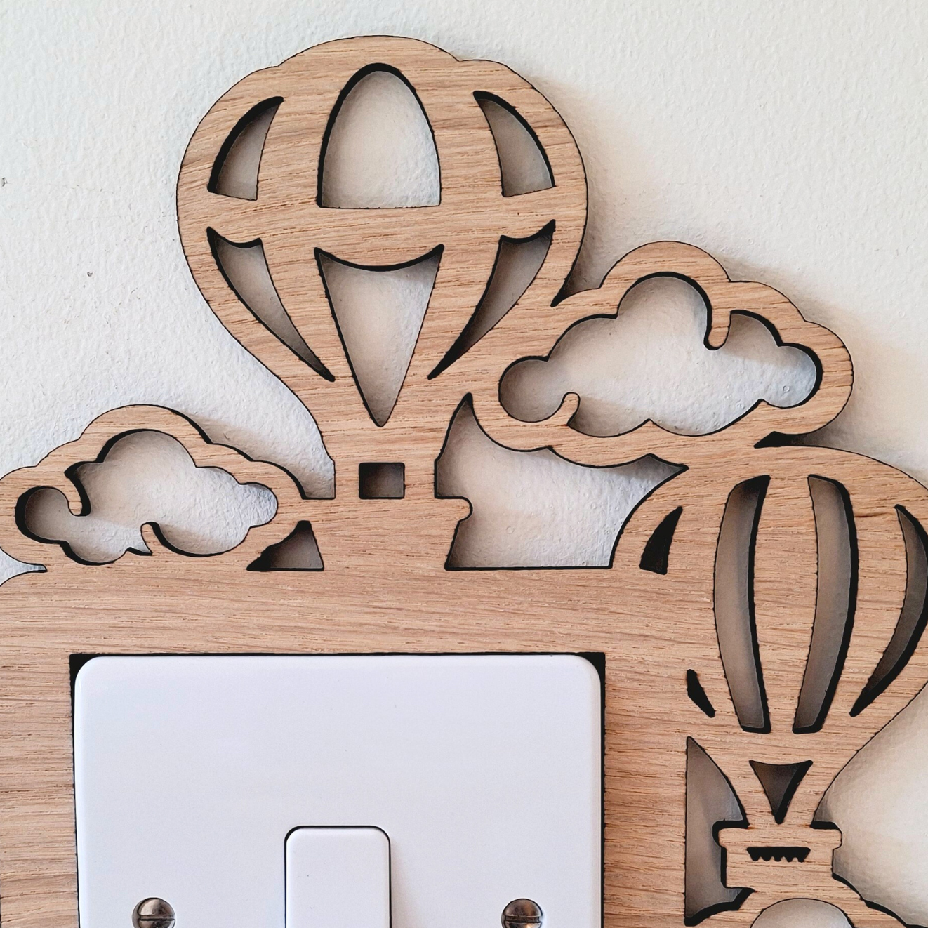 A wooden light switch with a decorative design featuring hot air balloons and clouds.
