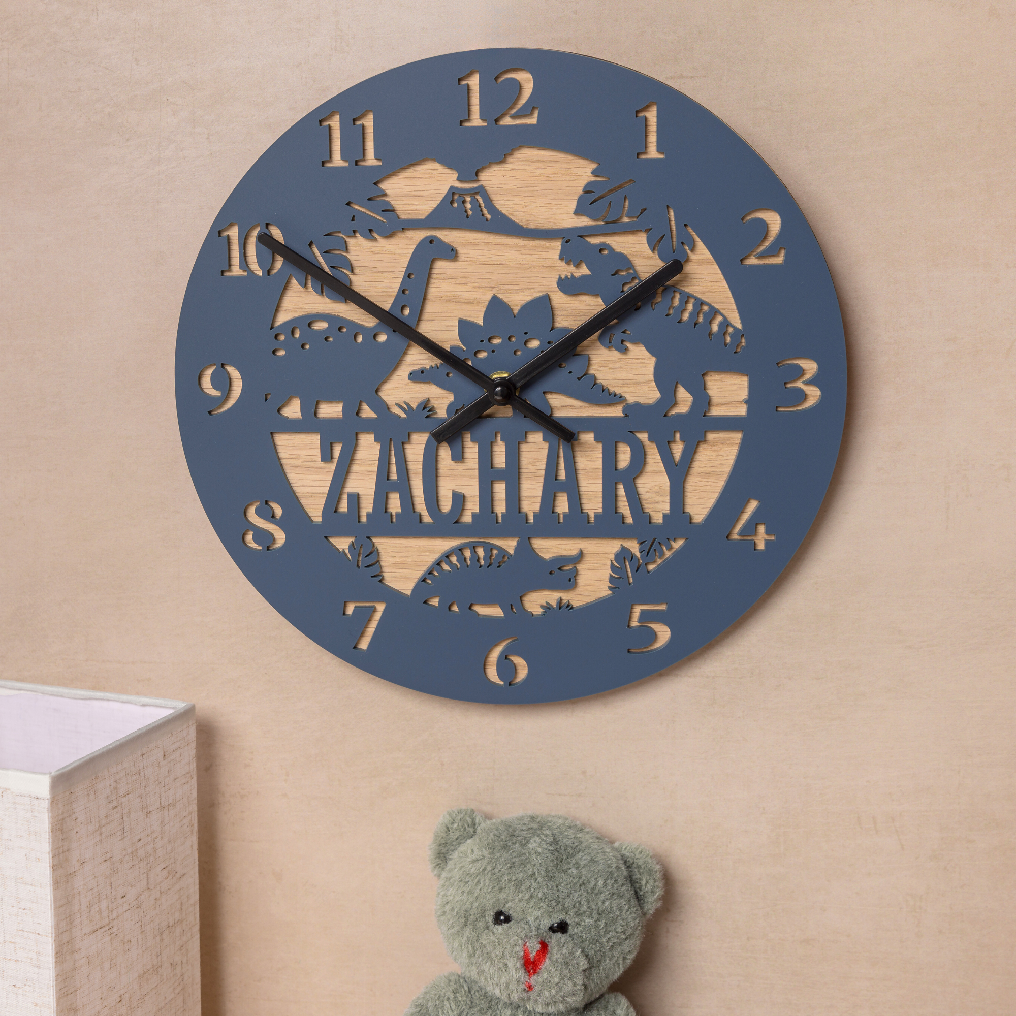 A wall clock with the name "ZACHARY" carved into it, along with a teddy bear and a lamp in the background.