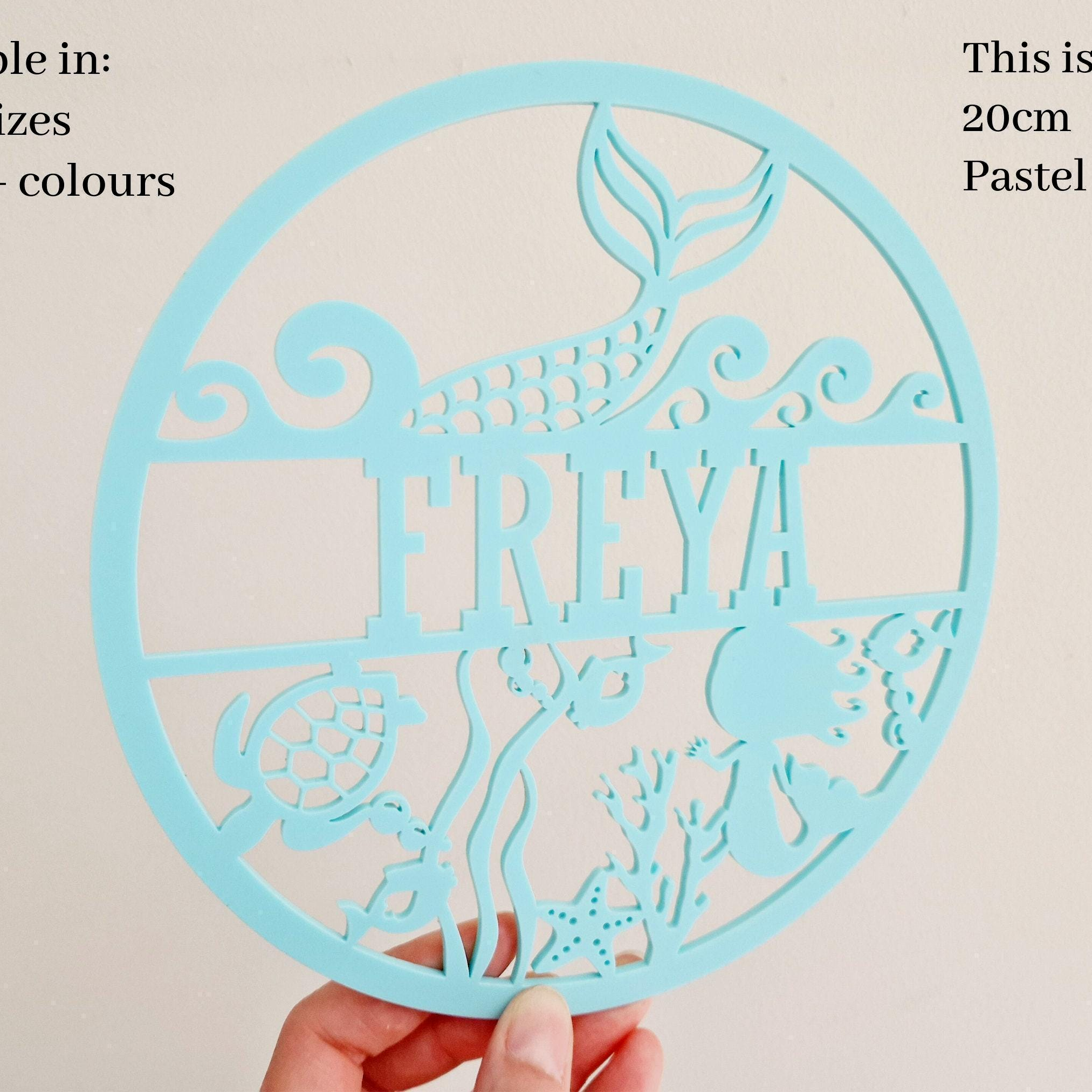 A hand holding a light blue circular cutout with the name "FREYA" written on it.