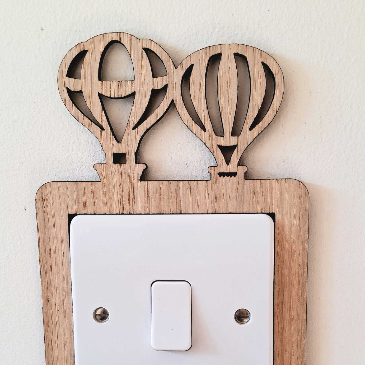 A wooden light switch with two hot air balloon-shaped cutouts on top.