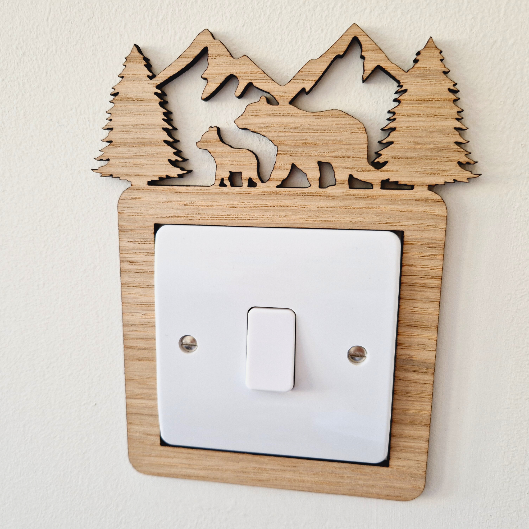 A wooden light switch with a carved design depicting a bear and pine trees on top.