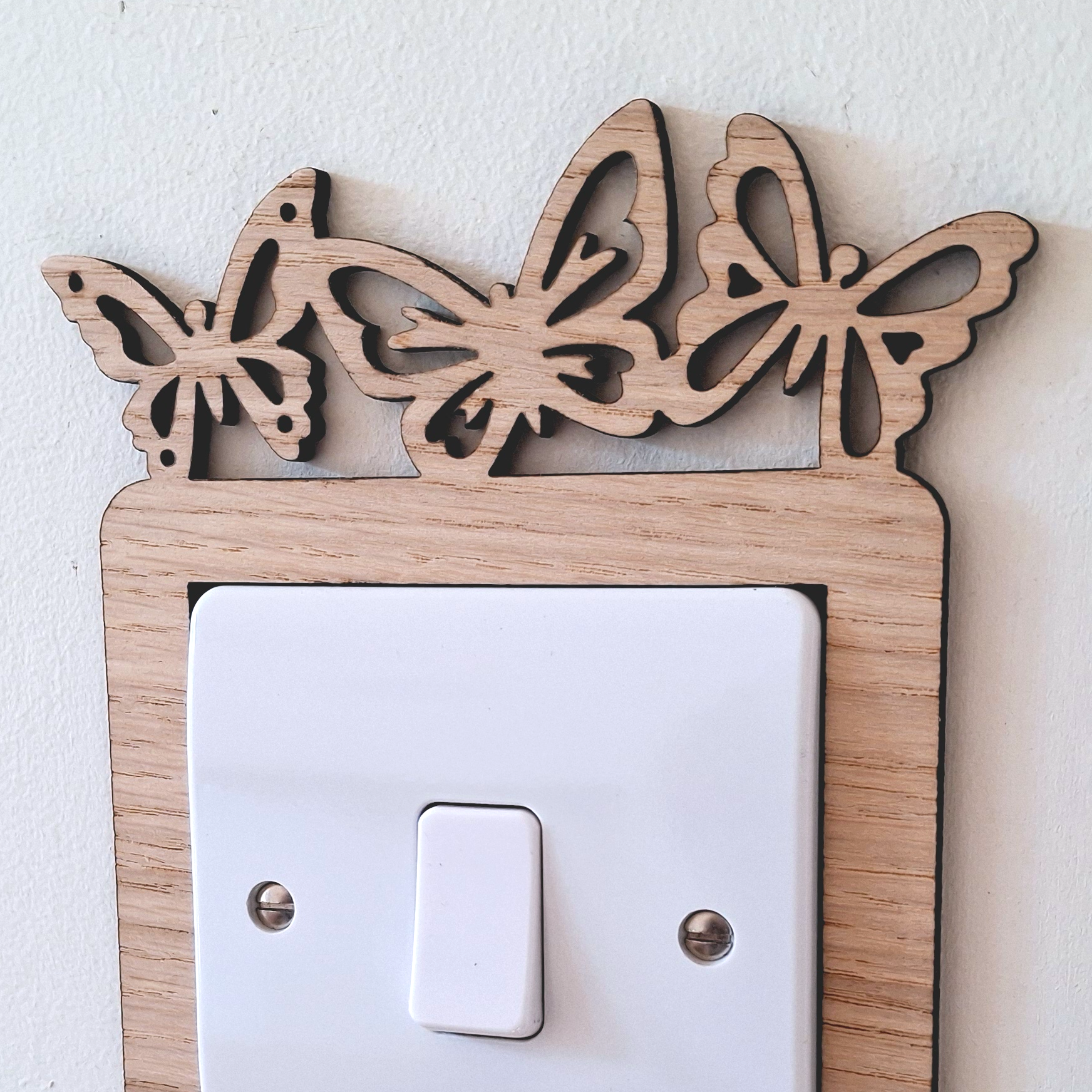 A wooden light switch with a butterfly design on the top and bottom edges, mounted on a white wall.