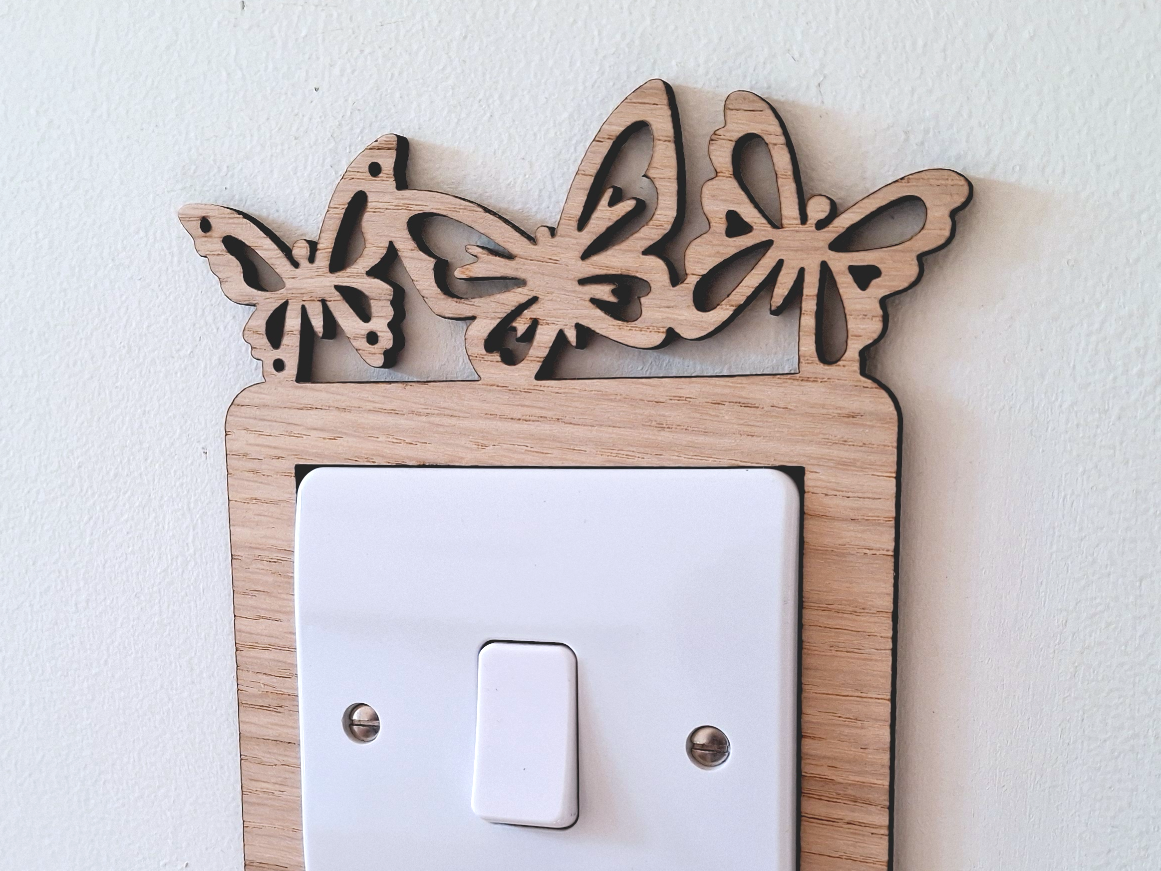 A wooden light switch with a butterfly design on the top and bottom edges, mounted on a white wall.