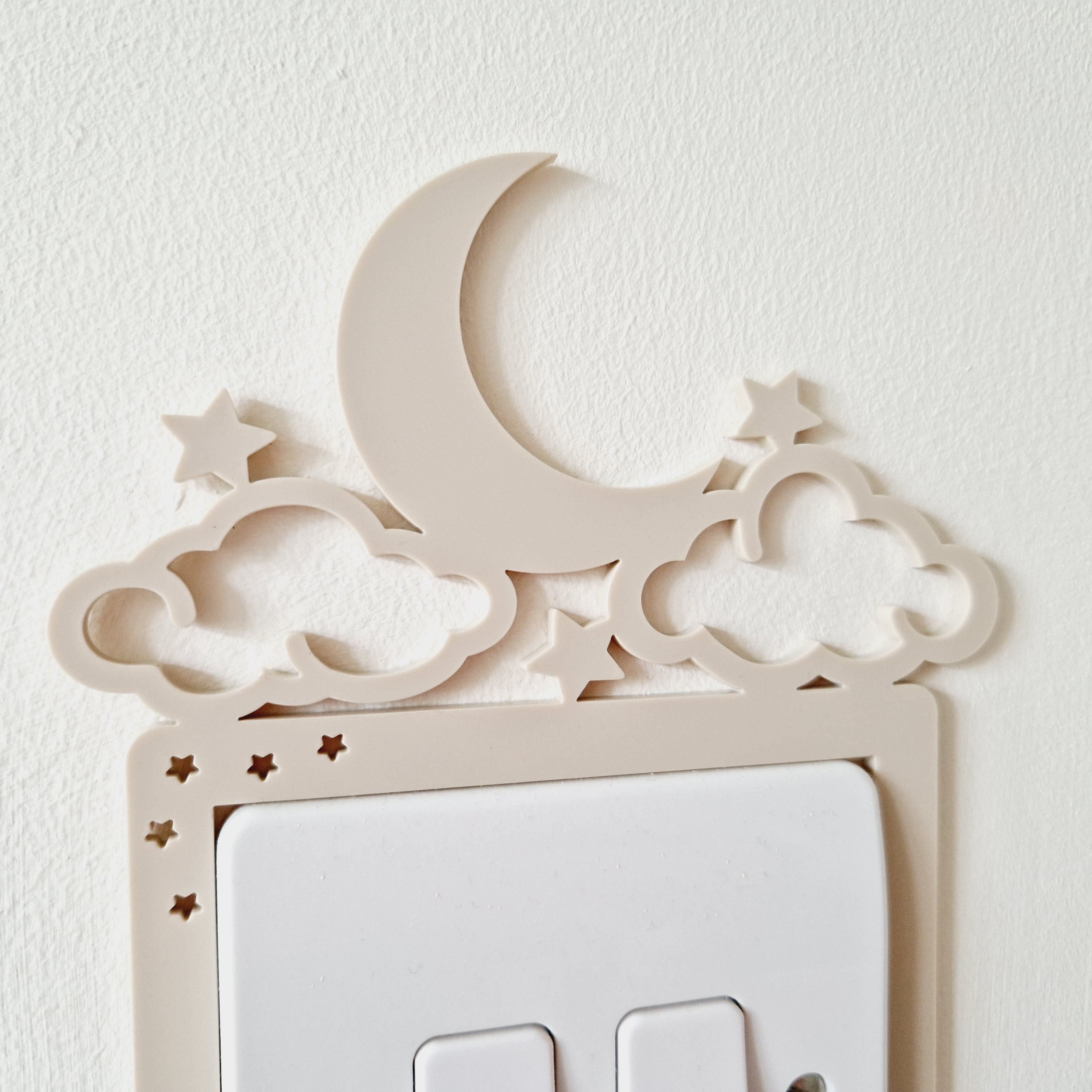 A wall-mounted light switch with a decorative crescent moon and star-shaped cutouts above it.
