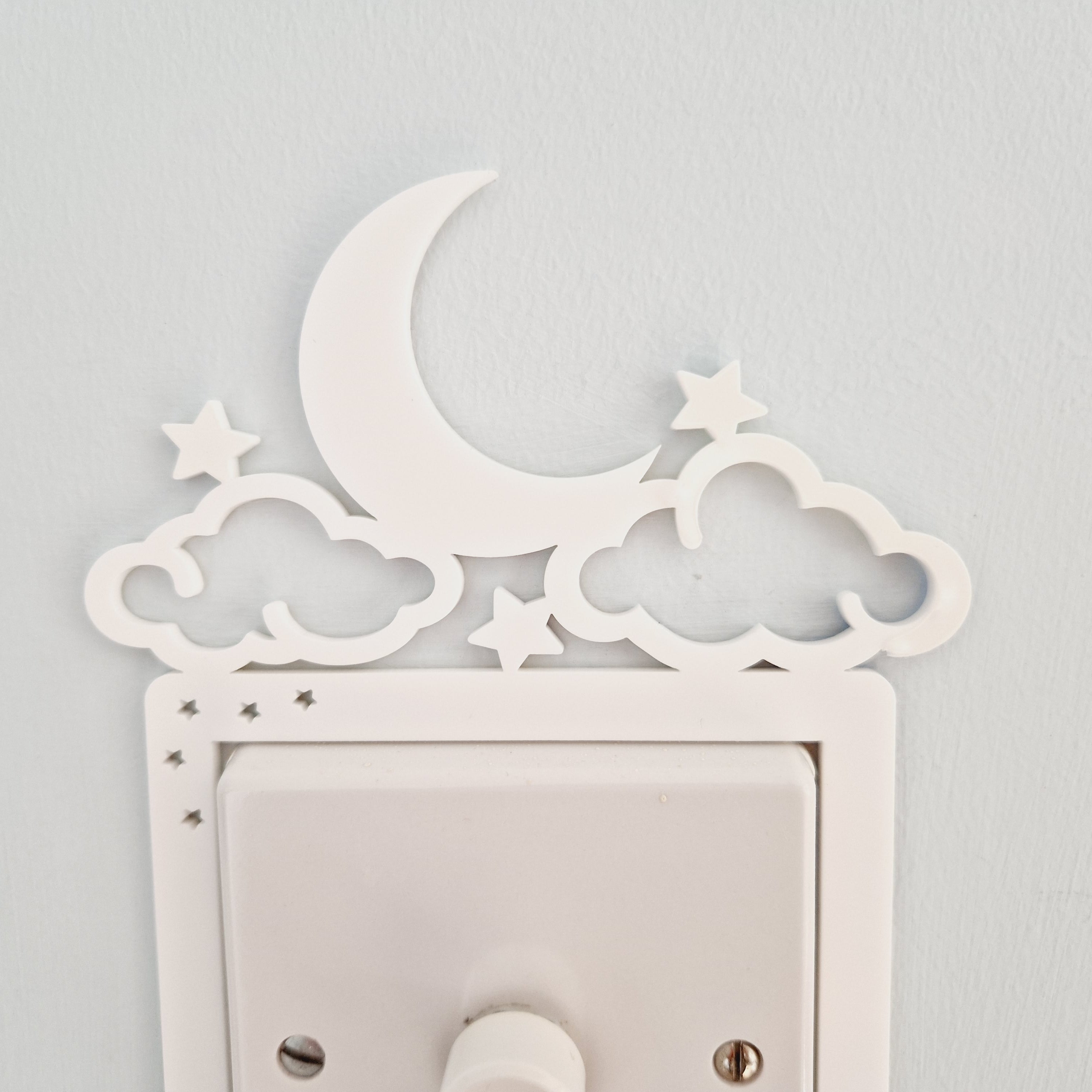 A white wall with a light switch and decorative moon and star-shaped cutouts.