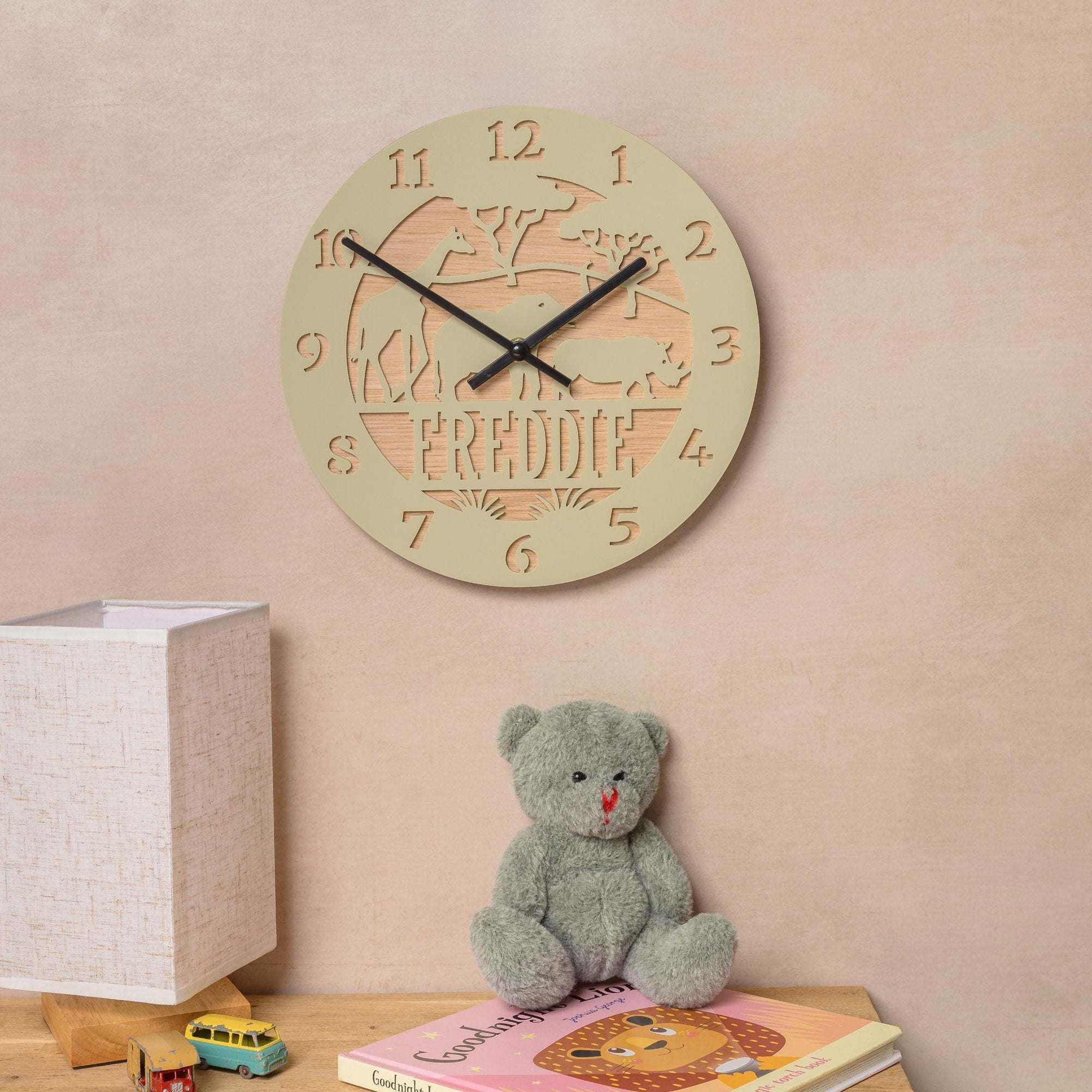 a wall clock with a giraffe design, a teddy bear, and a children's book on a wooden surface.