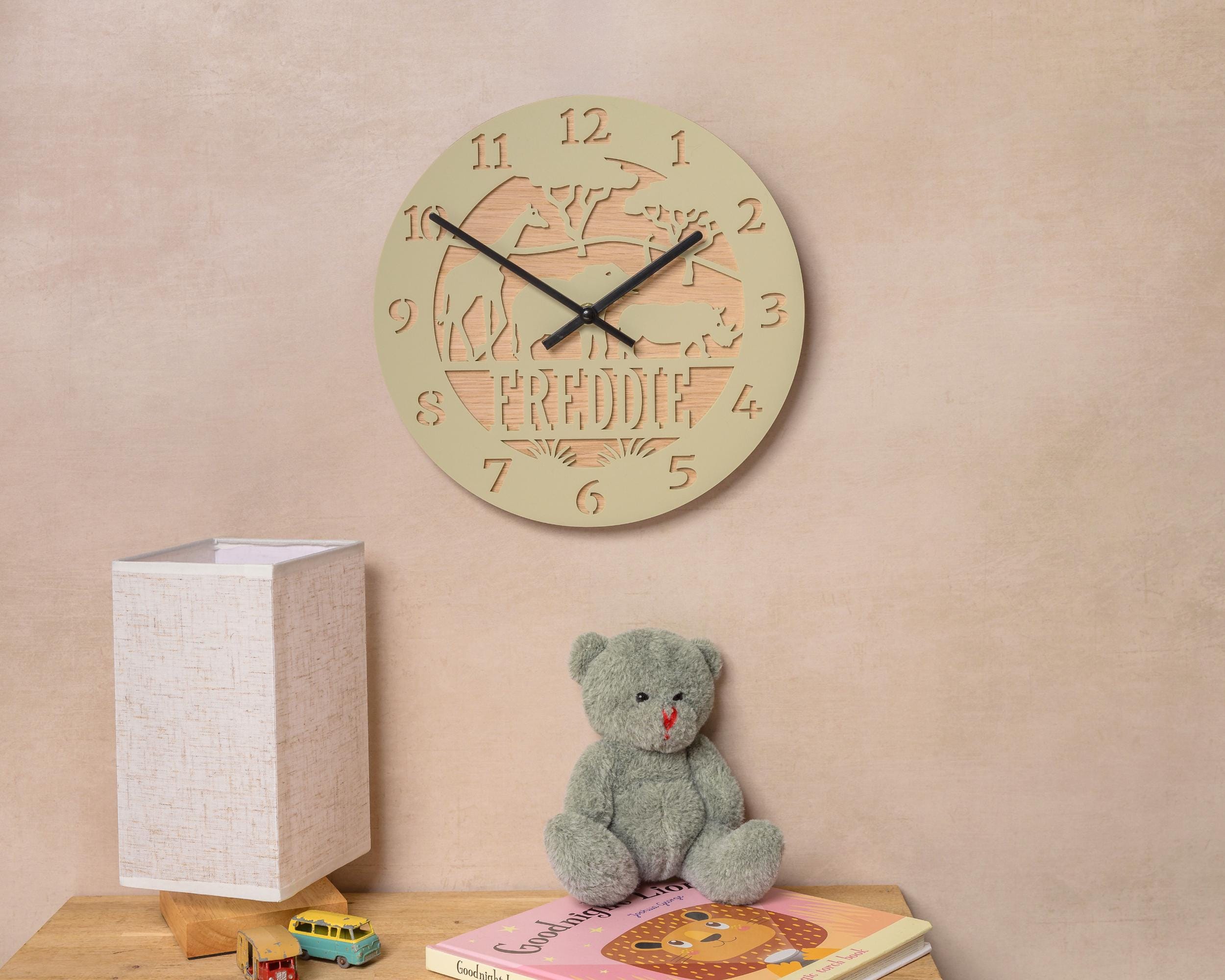 a wall clock with a giraffe design, a teddy bear, and a children's book on a wooden surface.