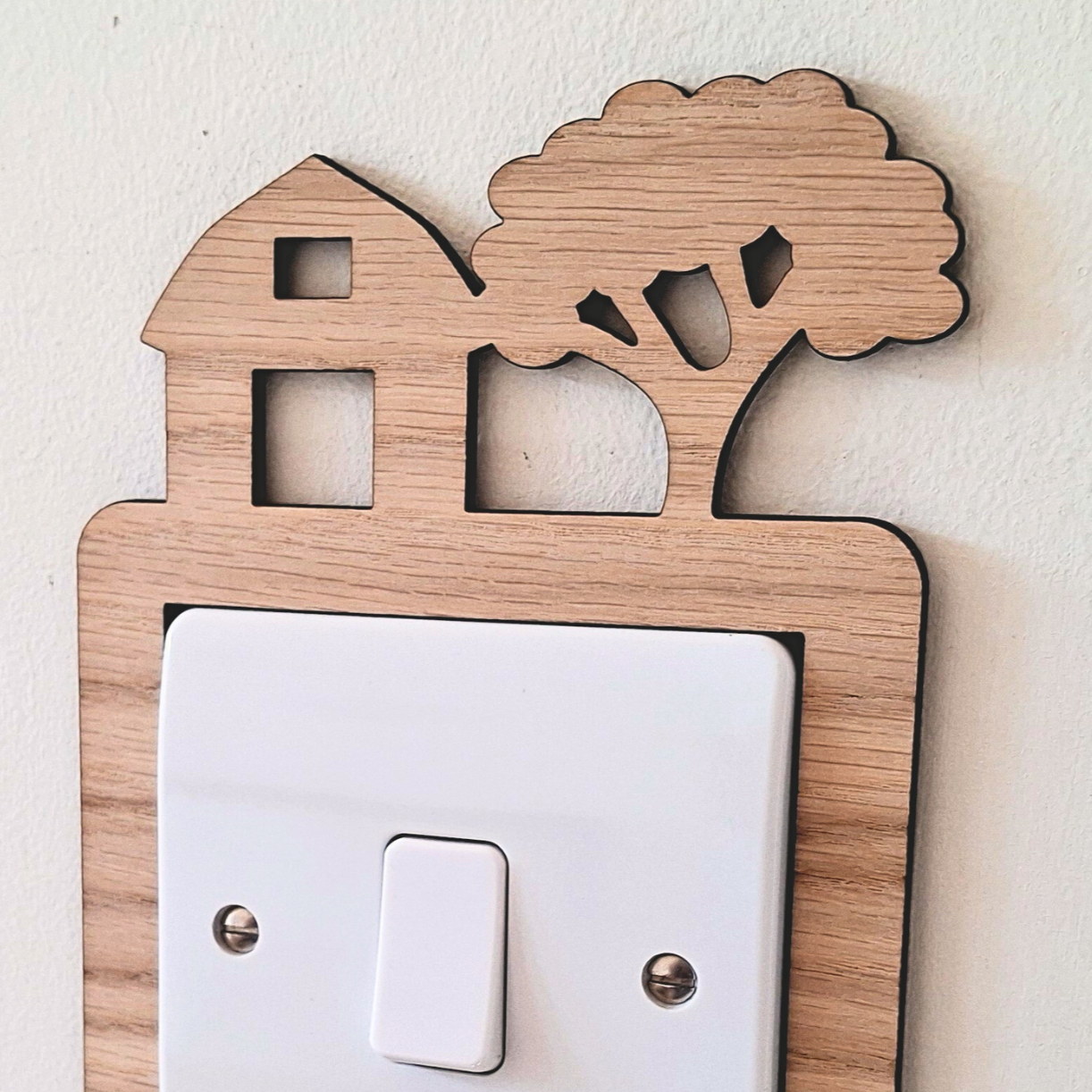 Decorative light switch cover with wooden frame and barn, tractor and tree design on a white wall.