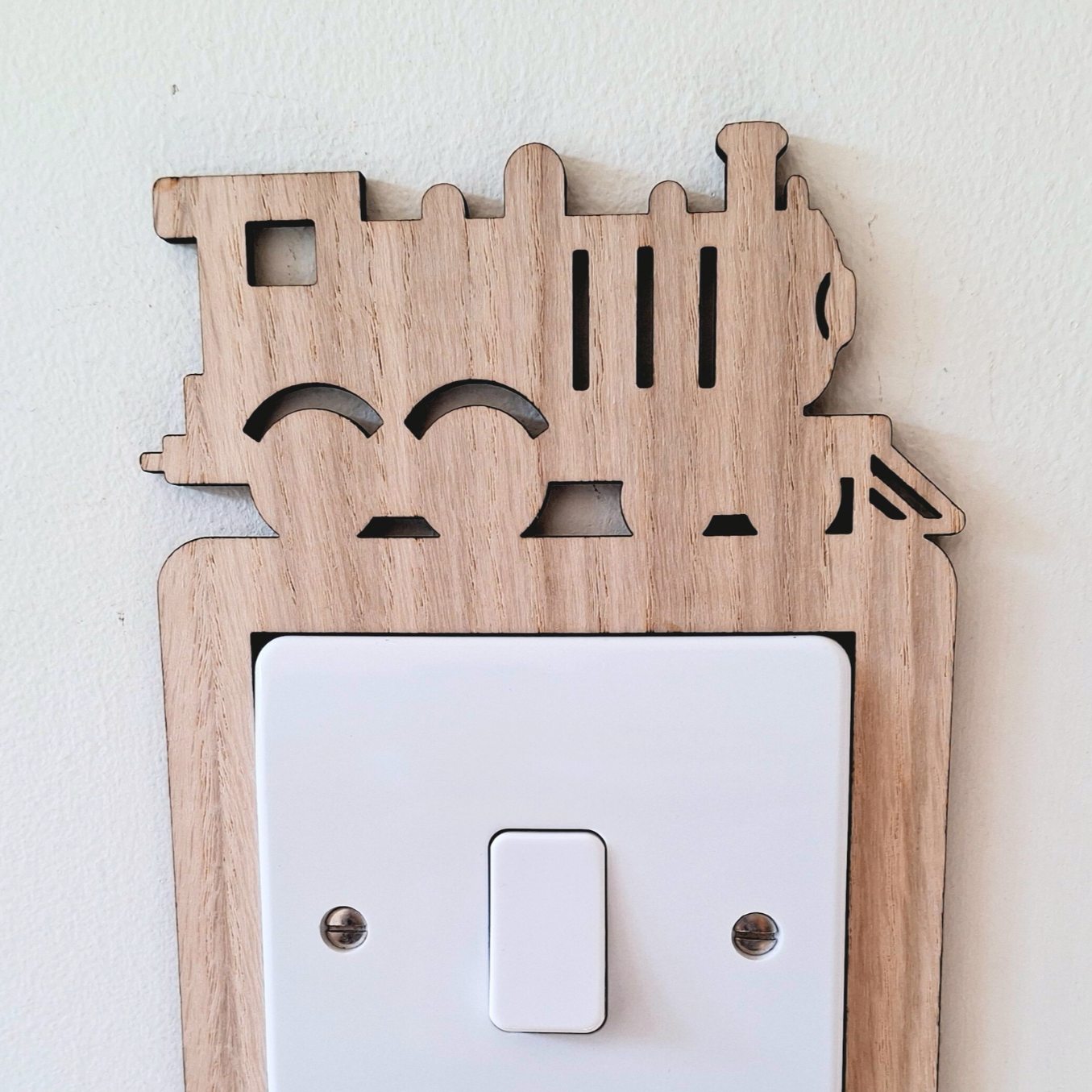 Wooden decorative switch cover with steam train cut-out designs on a white background