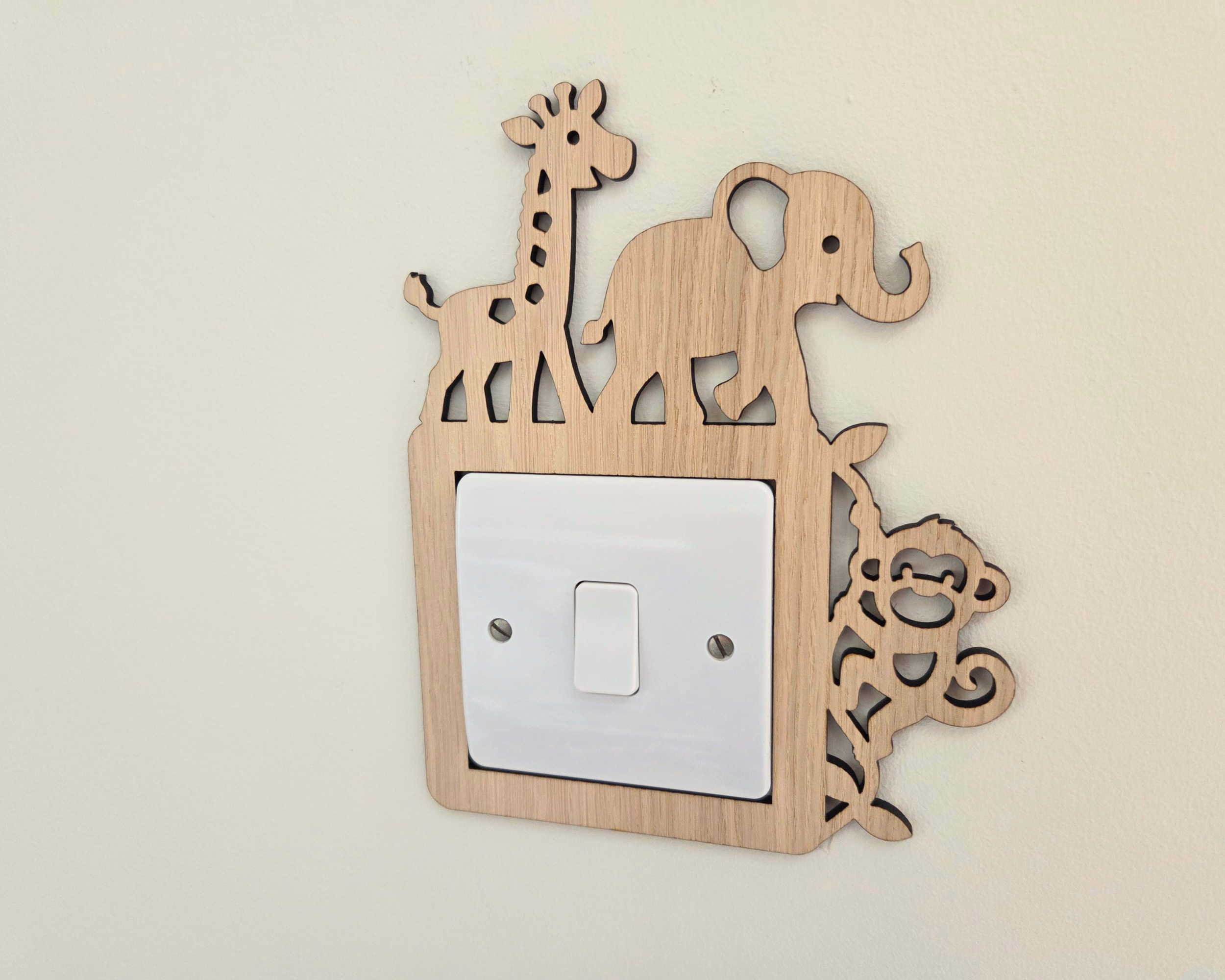 A light natural wood animal silhouette wall decor piece mounted on a beige wall, featuring a giraffe, elephant, and monkey design around a white single-toggle light switch plate.
