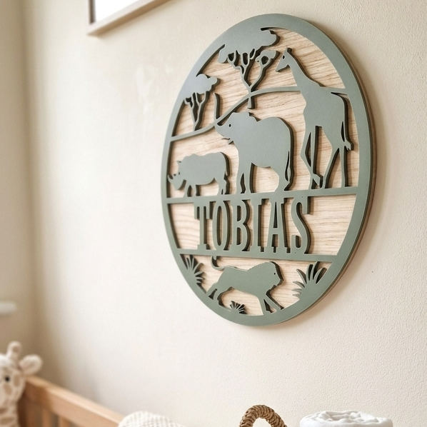 Round nursery name sign made from wood and acrylic featuring jungle animals and the name 'Tobias', above a crib, and basket of rolled up muslins.