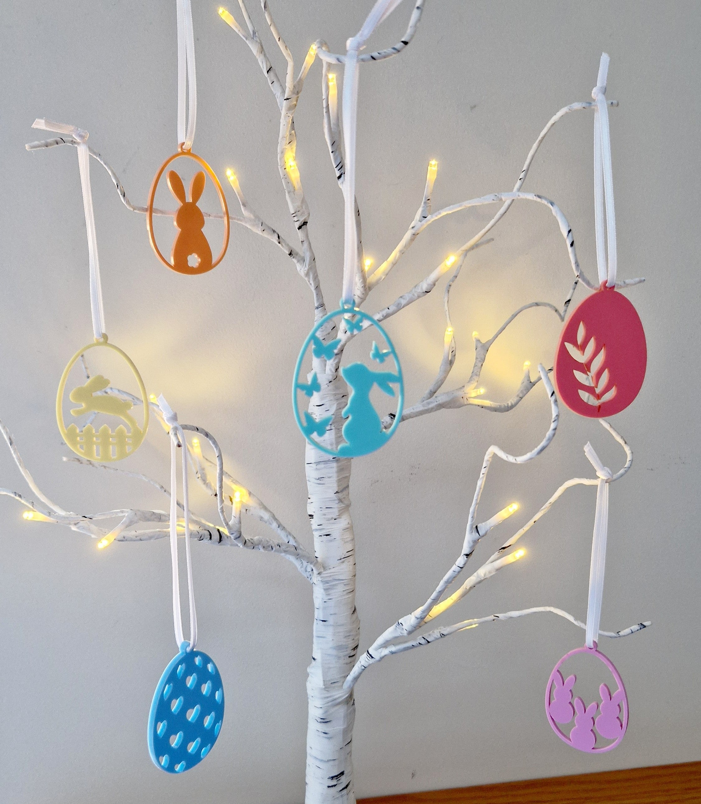 Decorative tree with colorful hanging easter themed ornaments on a white tree.