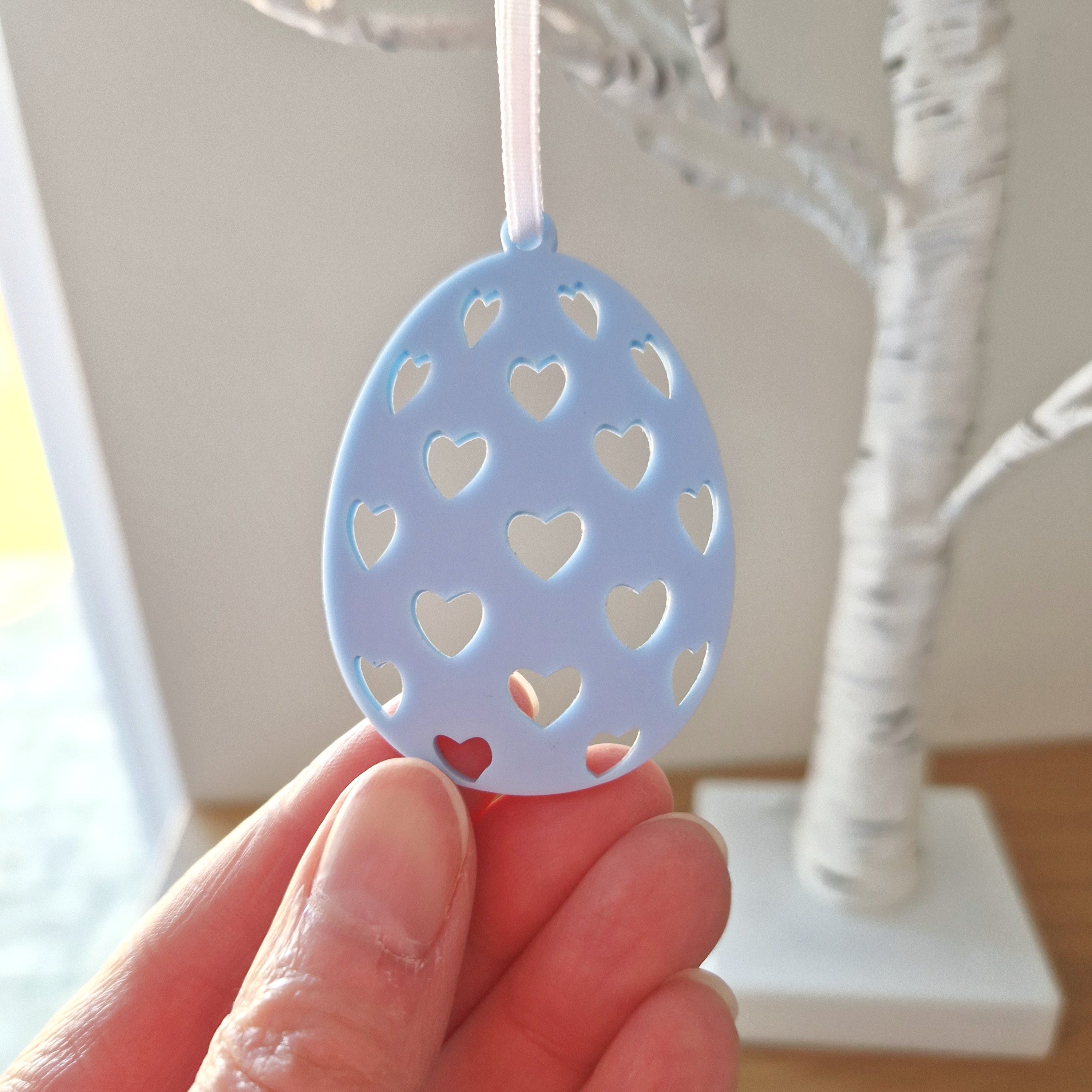 Blue decorative egg ornament with heart cutouts held by a hand against a neutral background