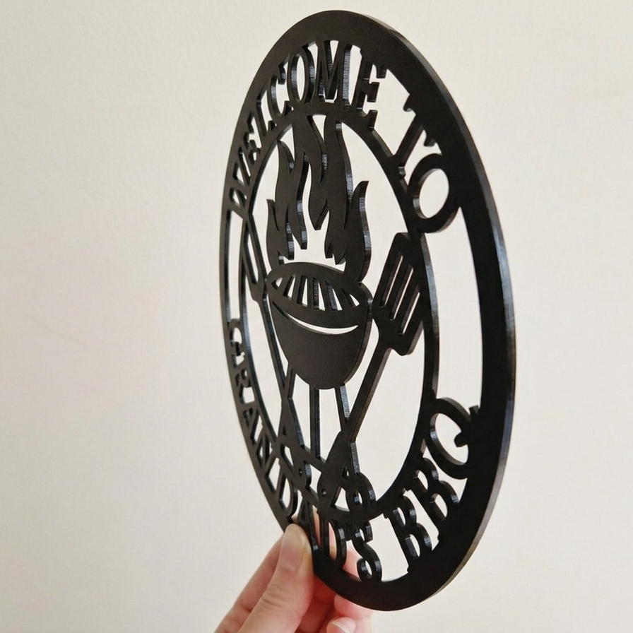 Side profile of decorative acrylic round sign with 'Welcome to the Grandad's BBQ' text and grill icon on a plain background