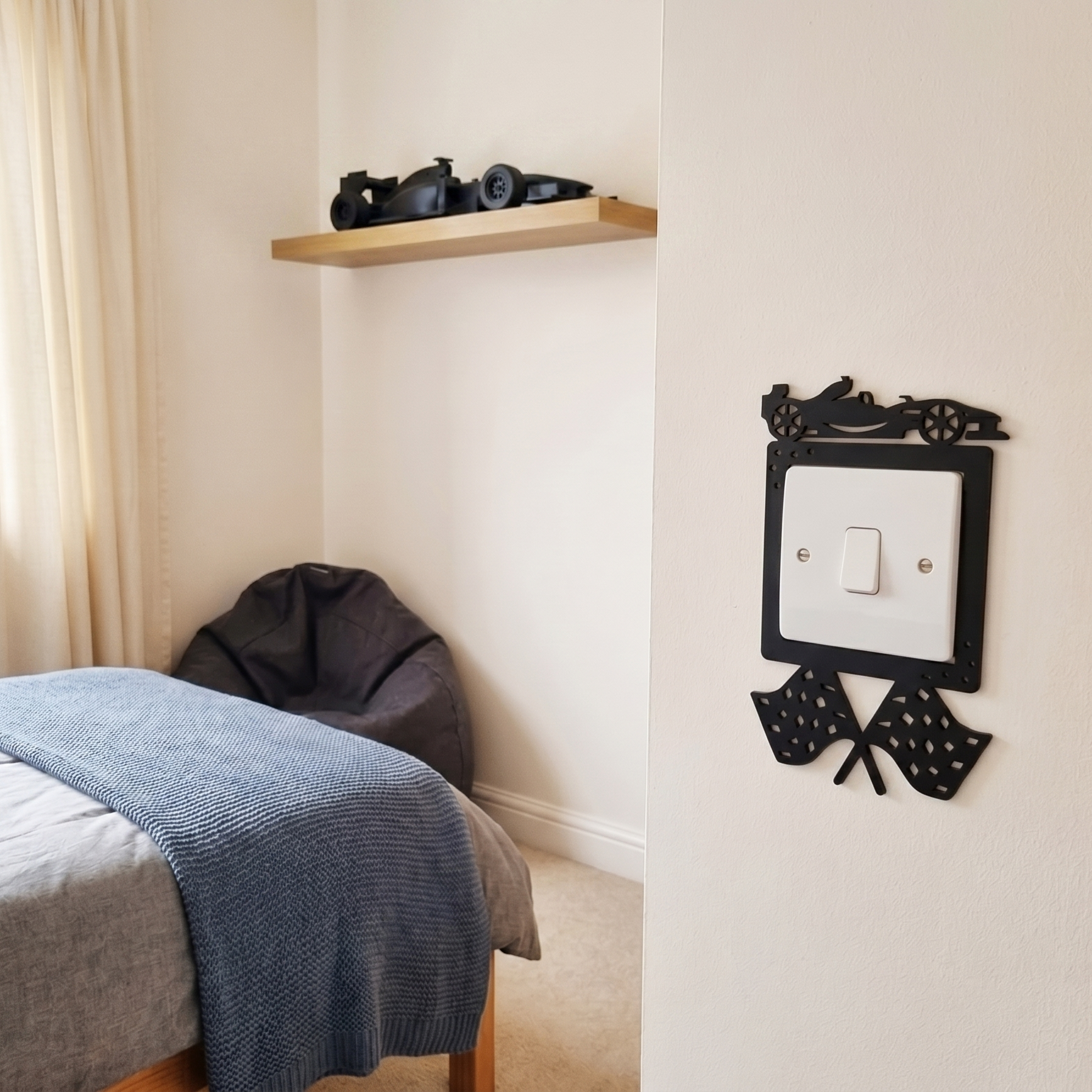 Bedroom with a bed, shelf, and decorative black racing car themed light switch cover.