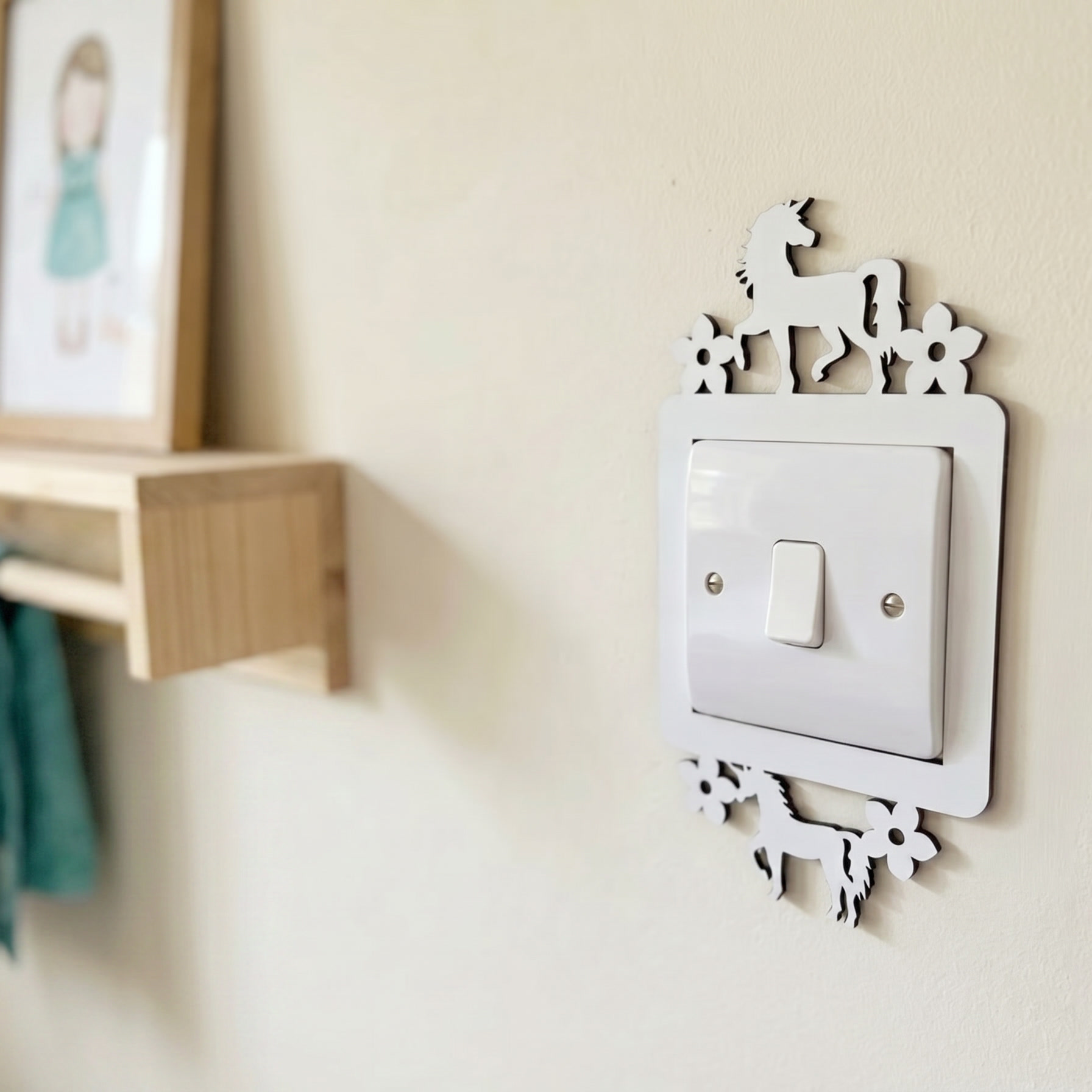 Decorative light switch cover with two unicorns and floral design on a wall next to a wooden shelf.
