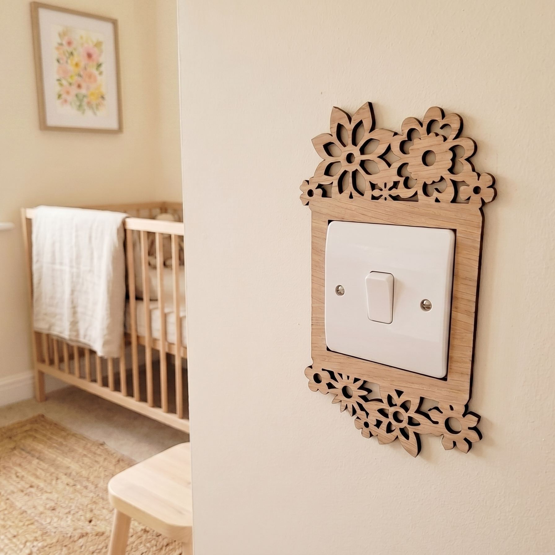Decorative wooden light switch cover with a daisy flower design, in a nursery setting with a crib and framed picture.