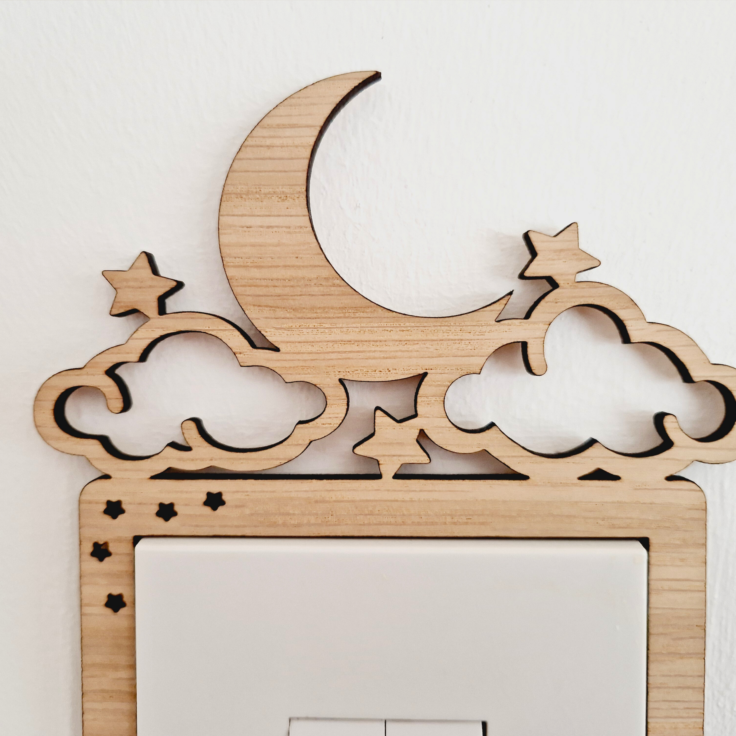 A wooden light switch with a crescent moon and stars carved into it, mounted on a wall.