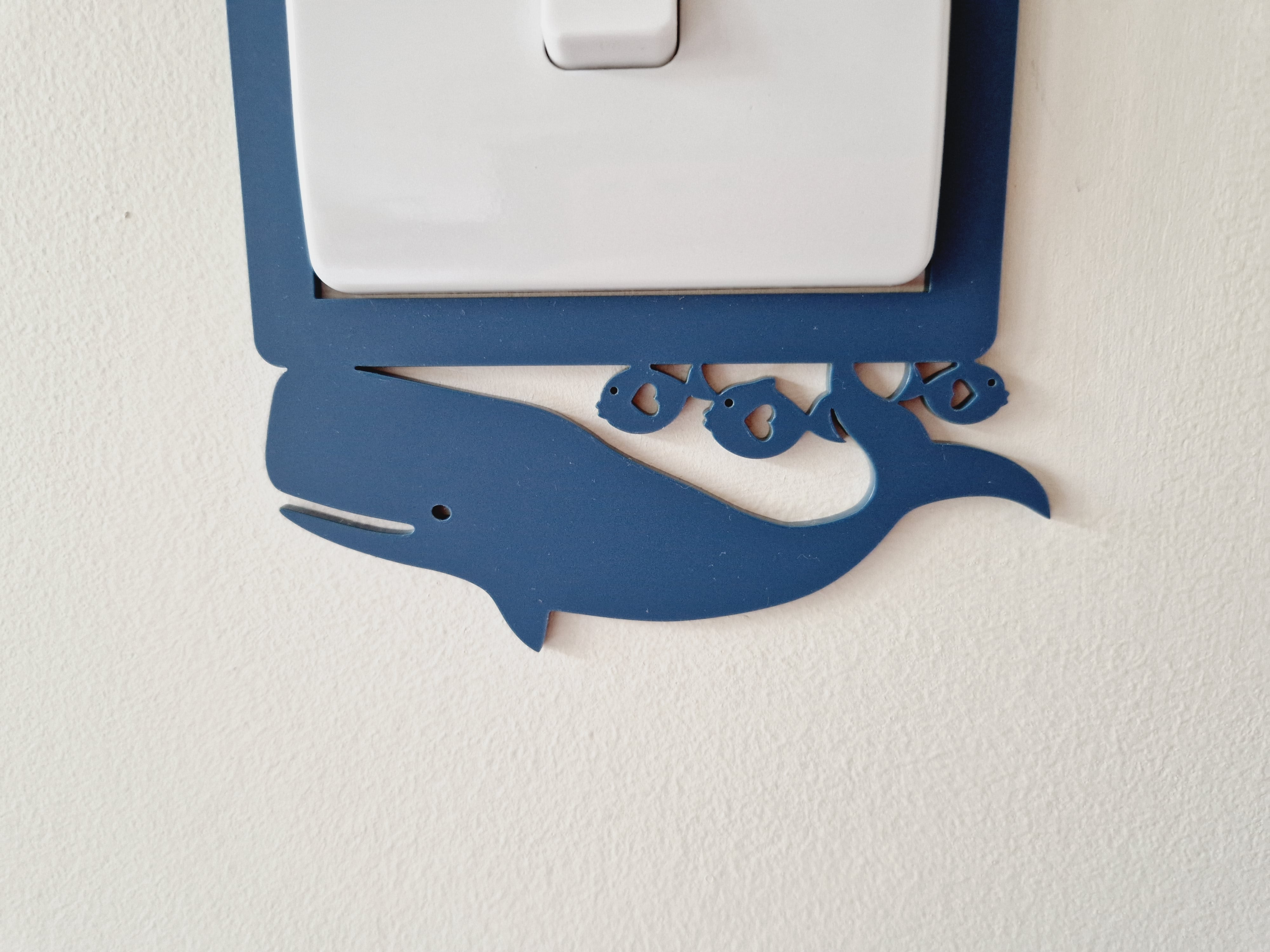 A light switch with a blue whale decoration on the plate.