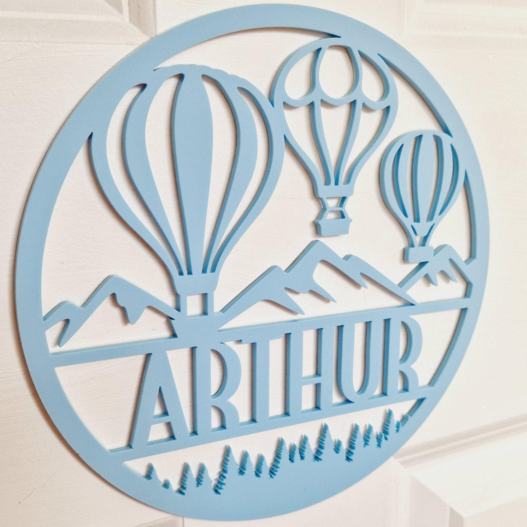 A light blue circular sign with a design featuring two hot air balloons and mountains.