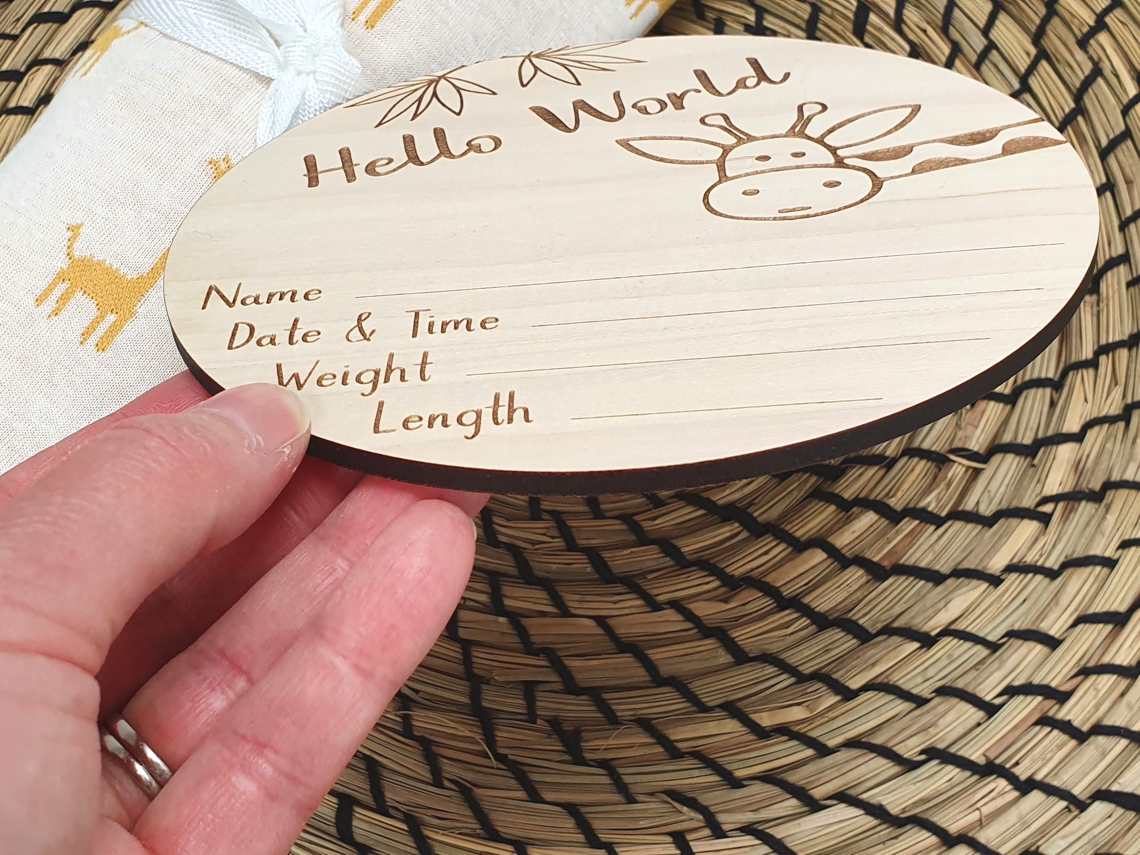 A wooden name tag with a giraffe design is being held by a person's hand, placed on a woven placemat.
