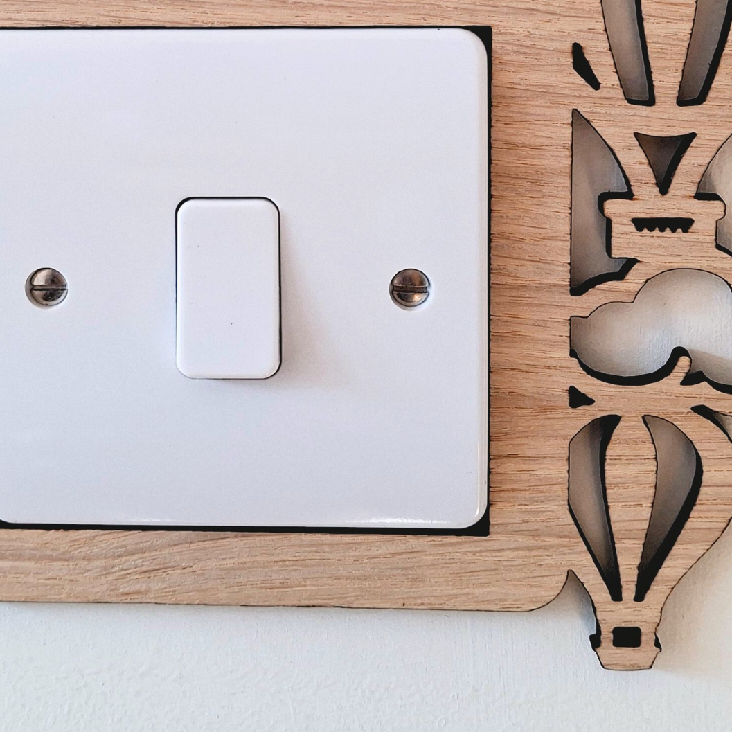 A wooden light switch with a decorative design featuring hot air balloons and clouds.
