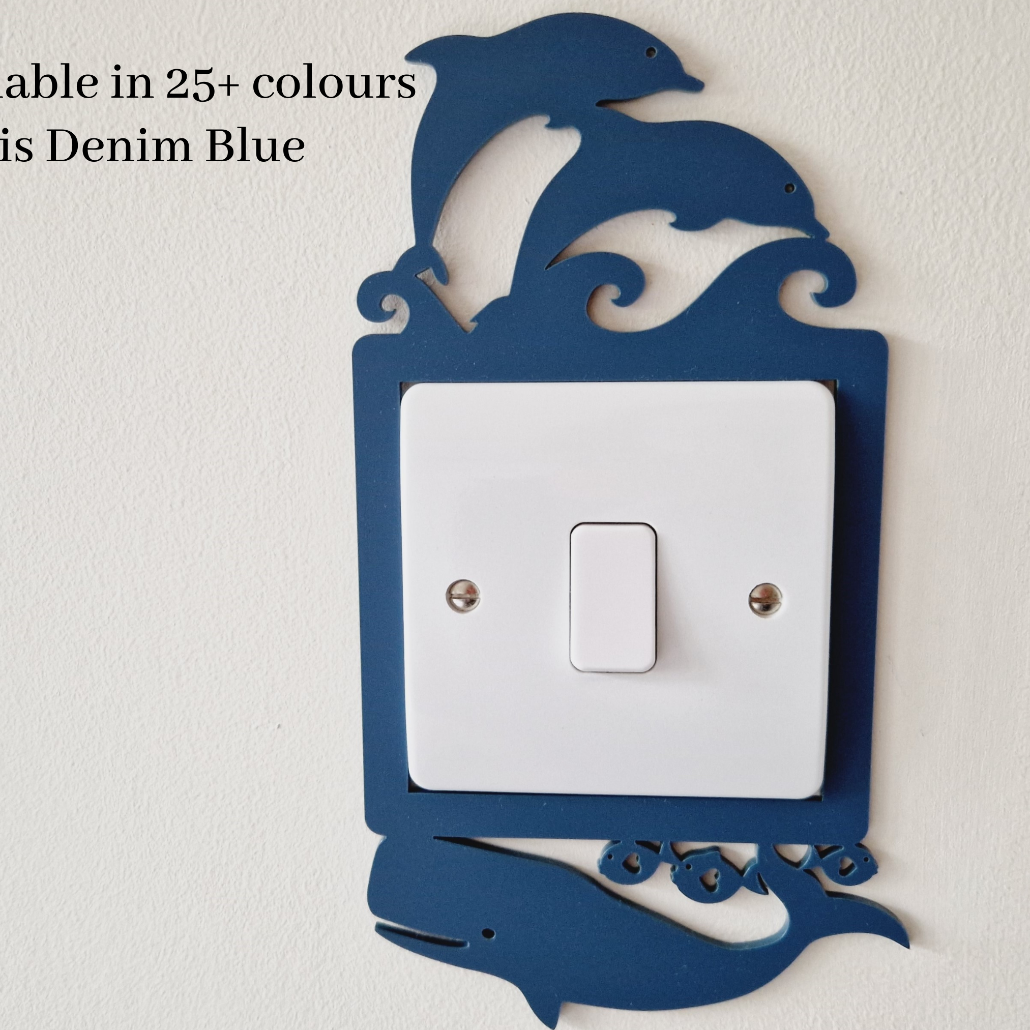 a light switch with a decorative design in the shape of a dolphin. The switch is mounted on a wall and is available in multiple colors, including denim blue.