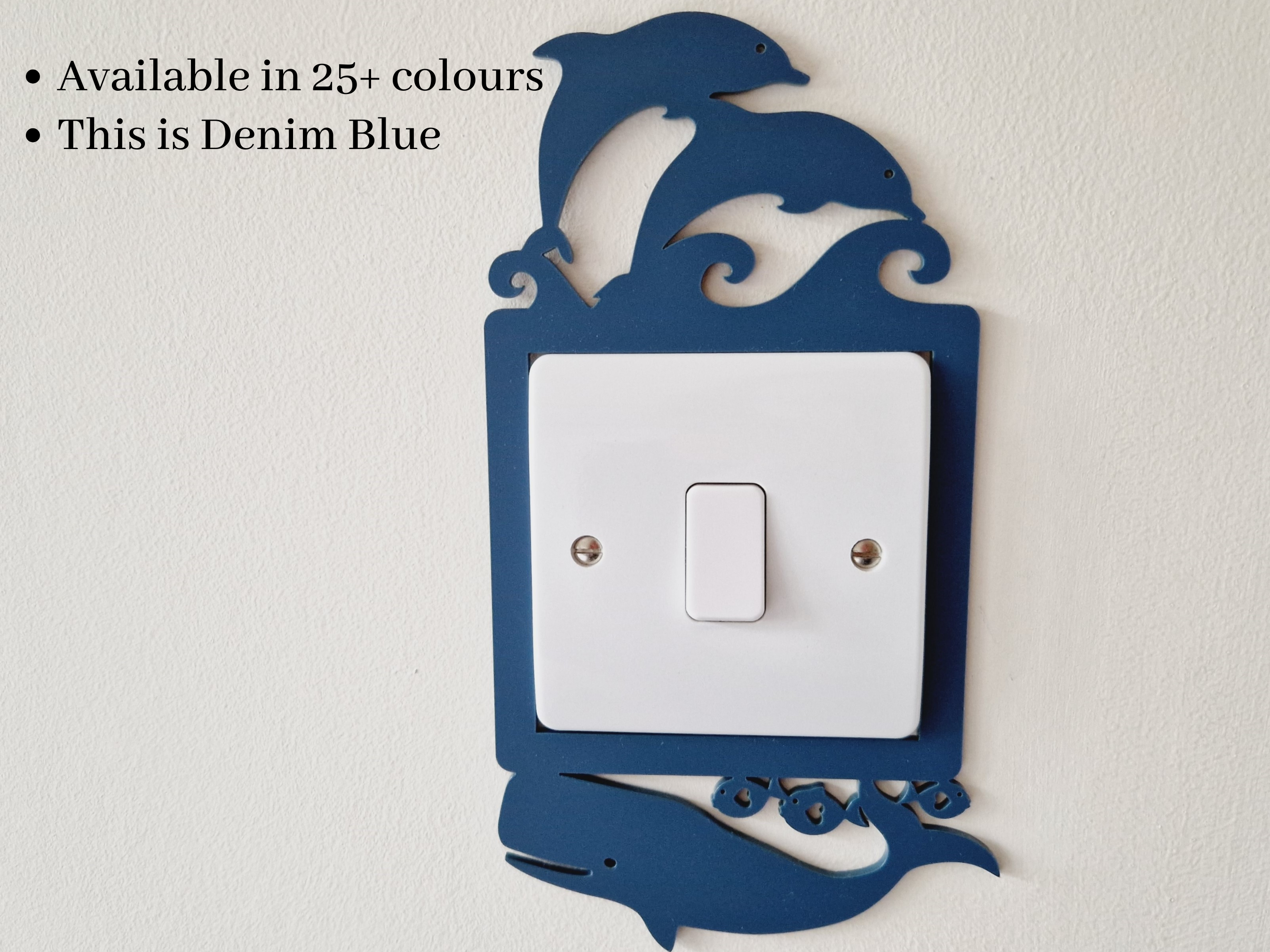 a light switch with a decorative design in the shape of a dolphin. The switch is mounted on a wall and is available in multiple colors, including denim blue.