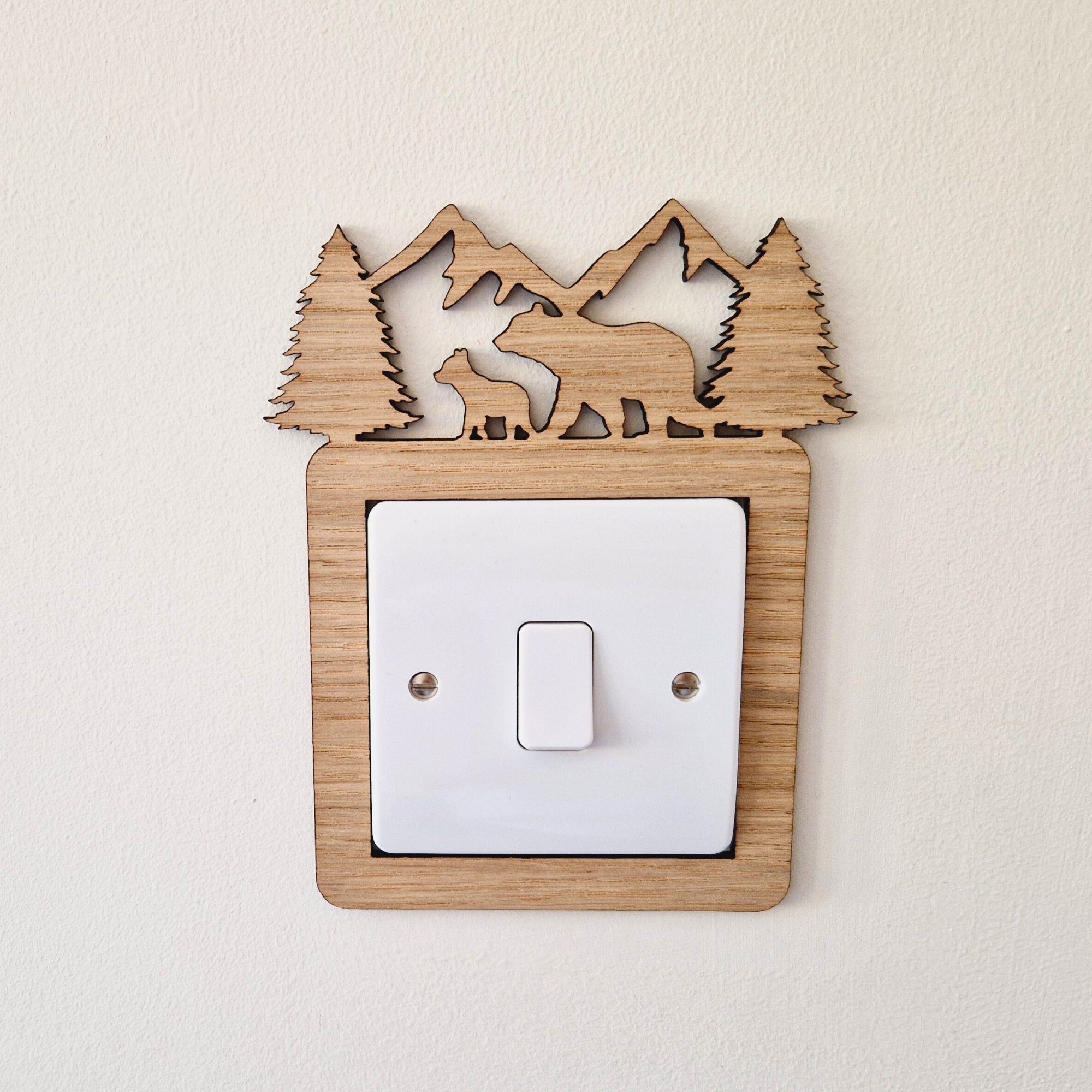 A wooden light switch with a carved design depicting a bear and pine trees on top.
