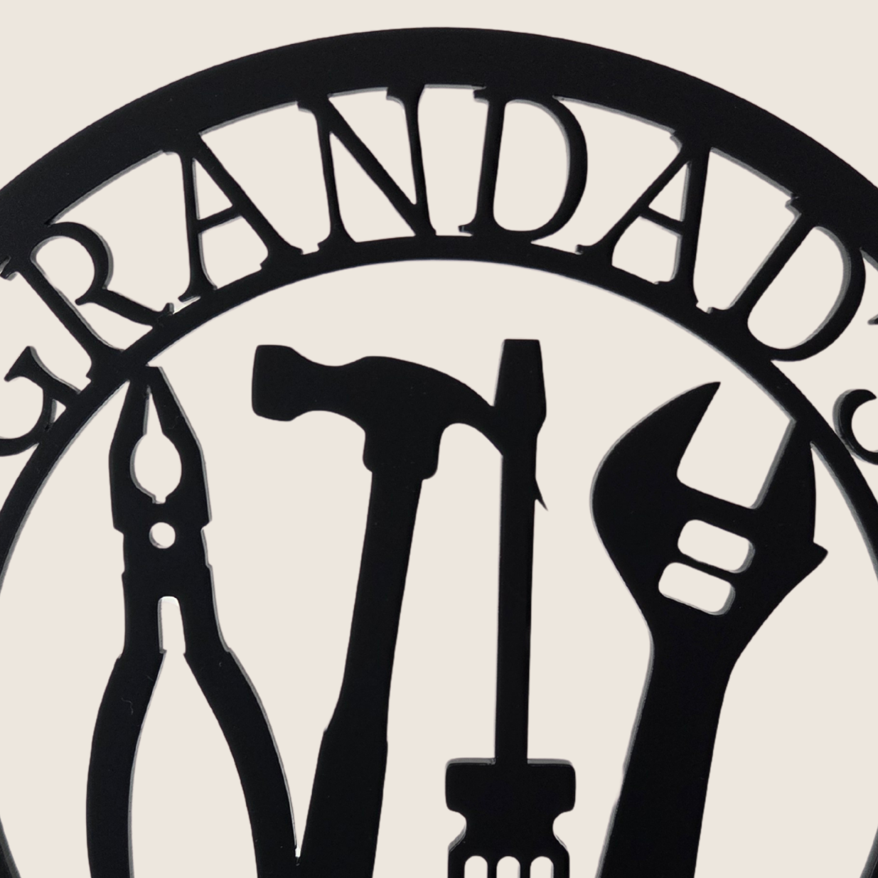 A hand holding a black metal sign with the text "GRANDDAD'S SHED" and various tools such as a hammer, wrench, and pliers.