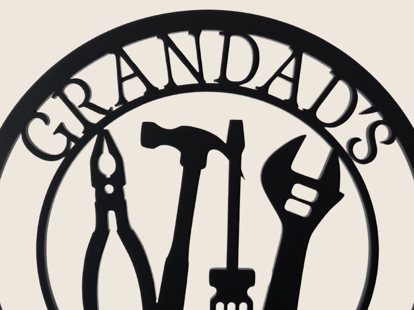 A hand holding a black metal sign with the text "GRANDDAD'S SHED" and various tools such as a hammer, wrench, and pliers.