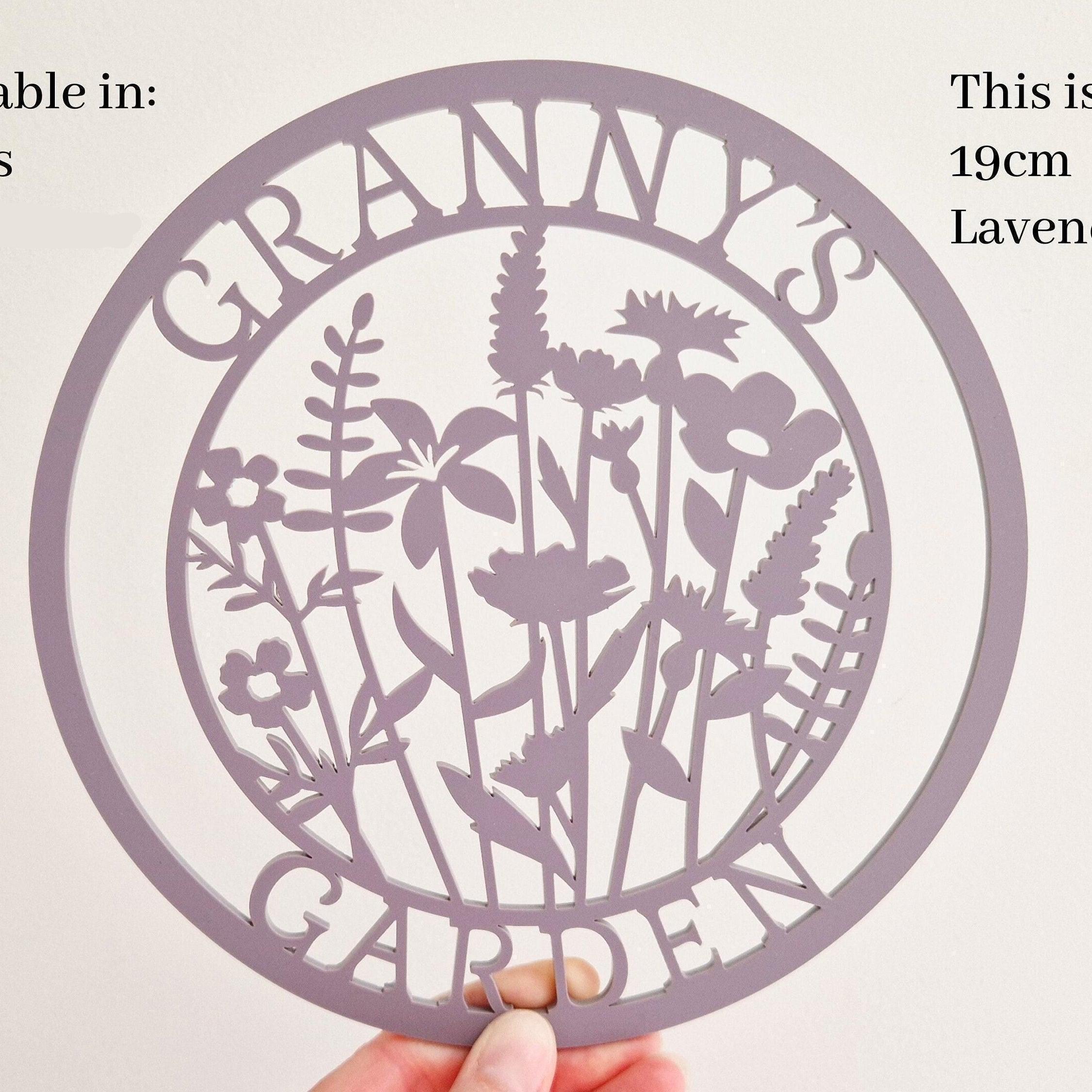 Decorative acrylic sign with floral design and 'Granny's Garden' text, held by a hand against a light background.