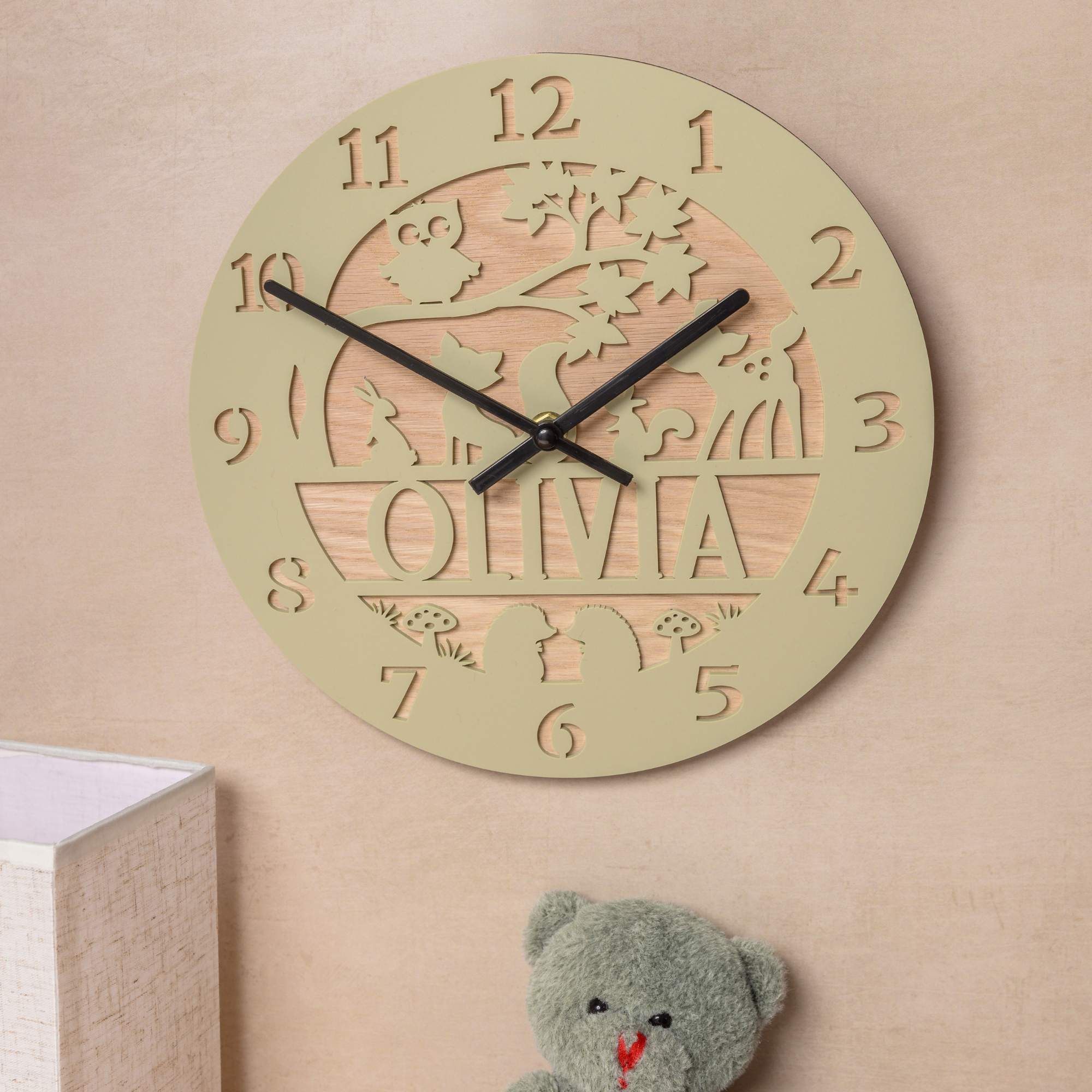 a round wooden clock with the name "Olivia" carved into it, hanging on a wall next to a stuffed teddy bear.