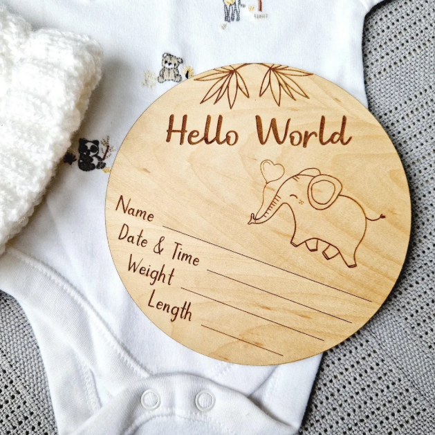 A wooden baby name card with a picture of an elephant and the text "Hello World" is placed on a white cloth.