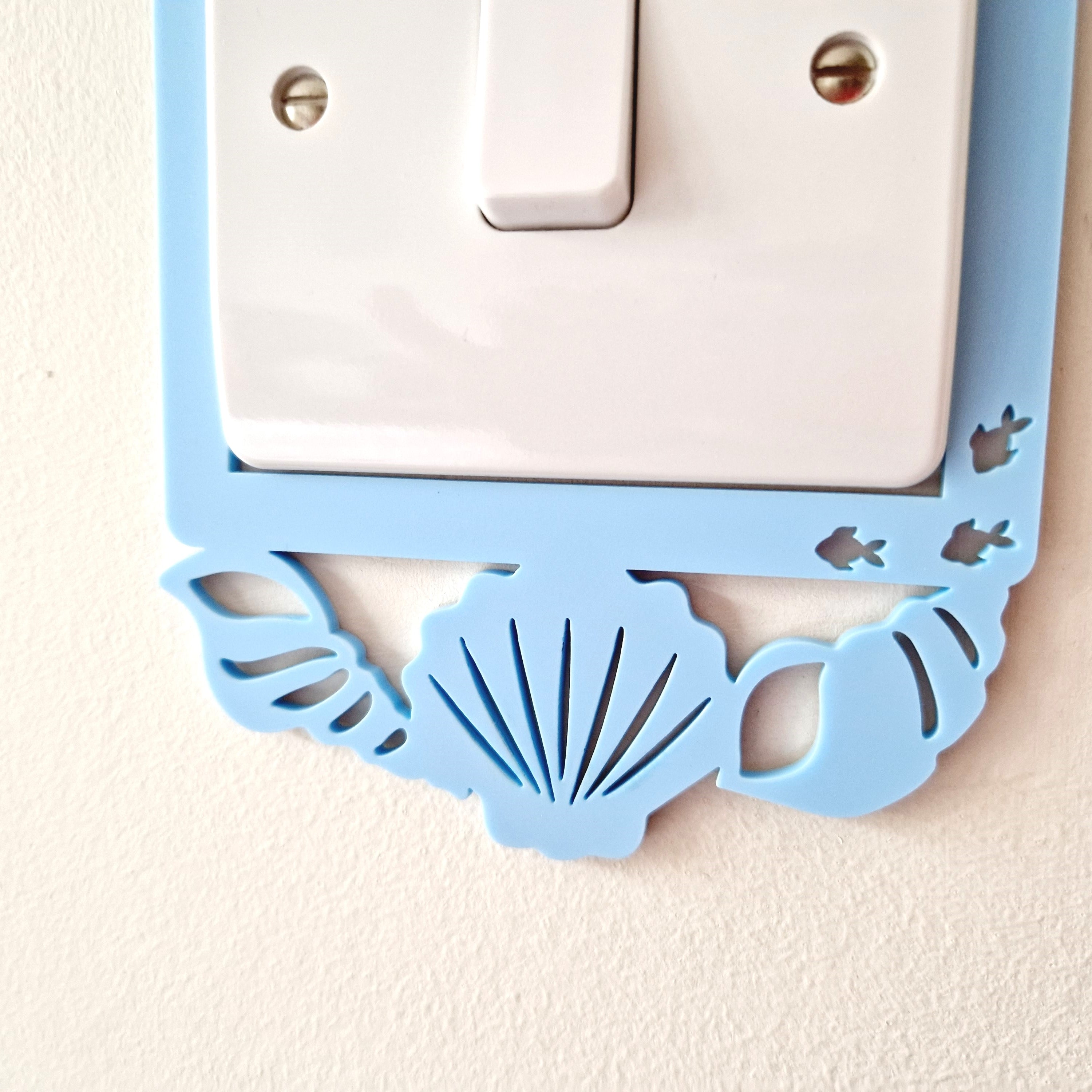 A light switch with a decorative blue frame featuring a seashell and fish design.