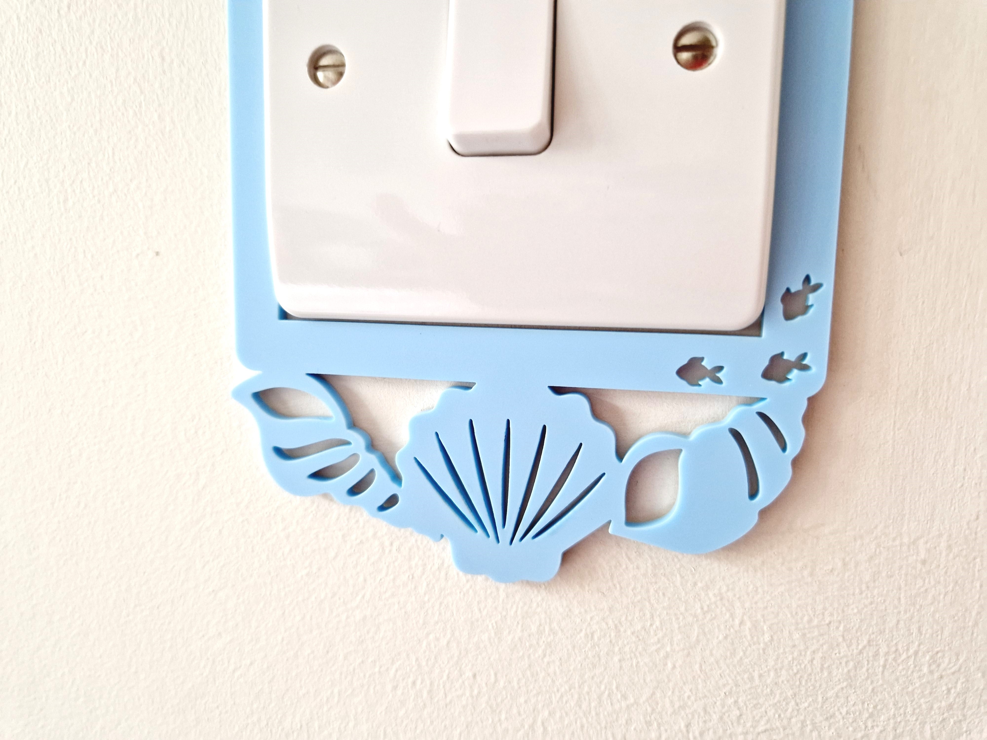A light switch with a decorative blue frame featuring a seashell and fish design.