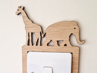 A wooden light switch with a giraffe and elephant silhouette on top, mounted on a white wall.
