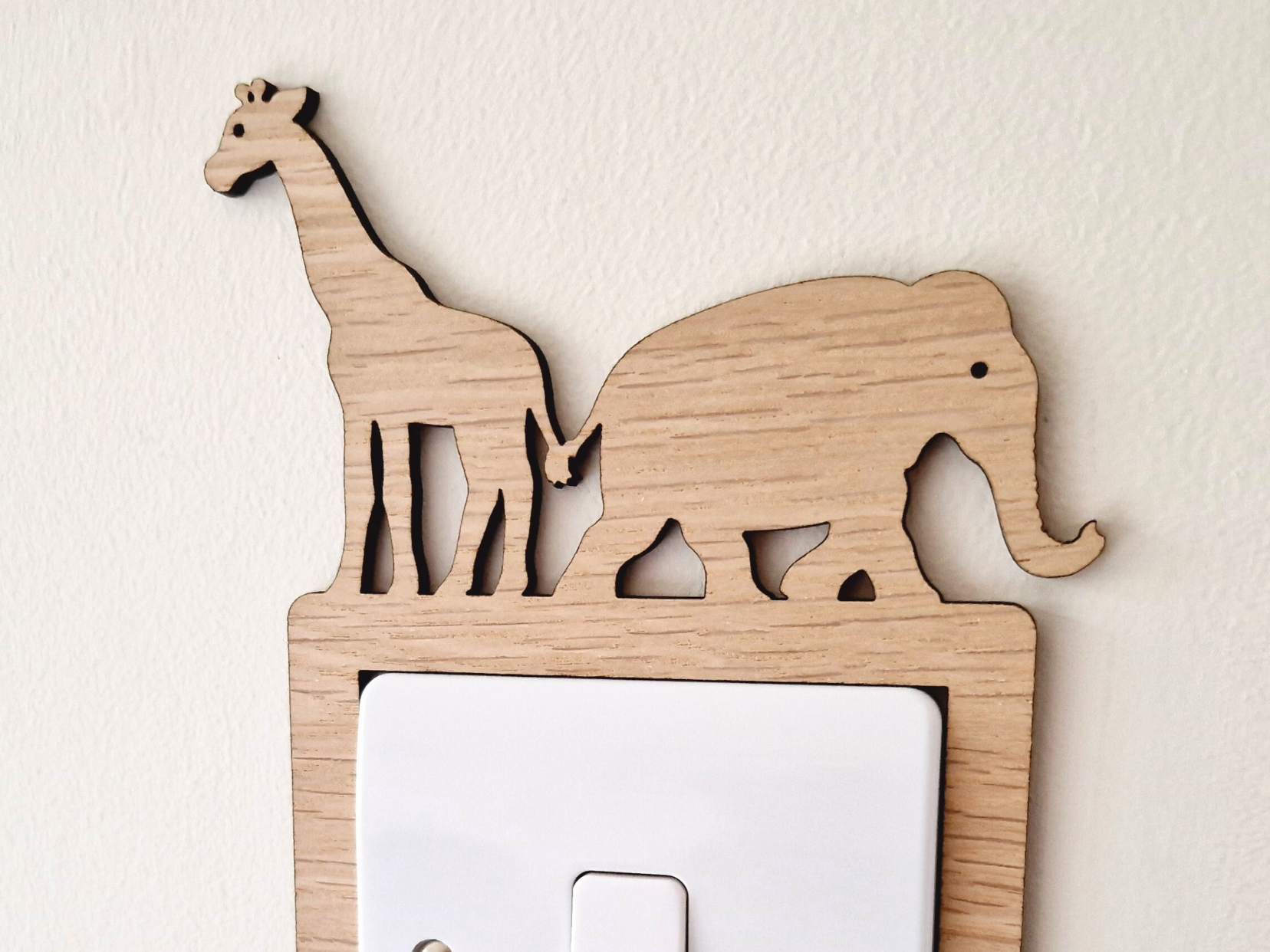 A wooden light switch with a giraffe and elephant silhouette on top, mounted on a white wall.